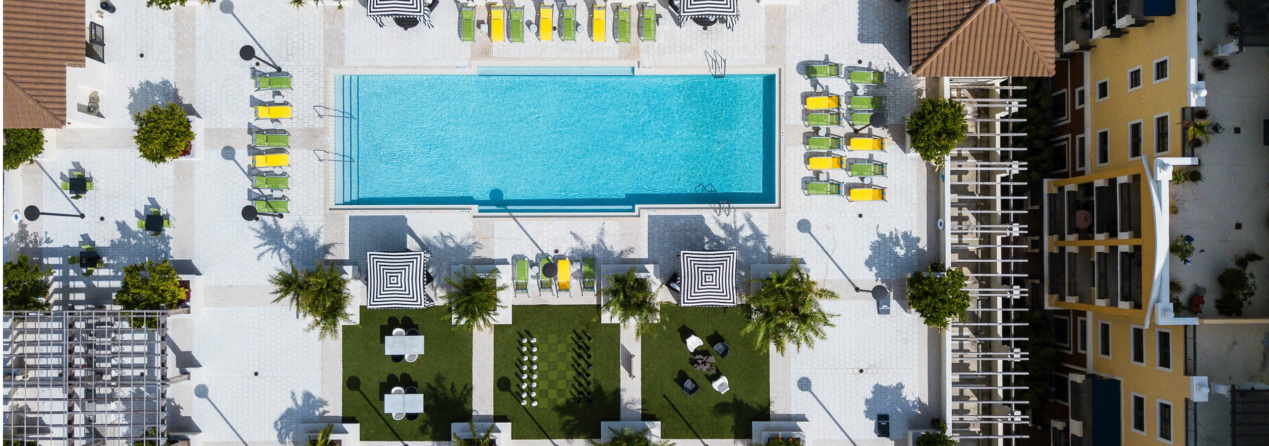 Aerial Rooftop view of the AMLI Dadeland Pool with black and white cabanas, outdoor games, green and yellow lounge chairs