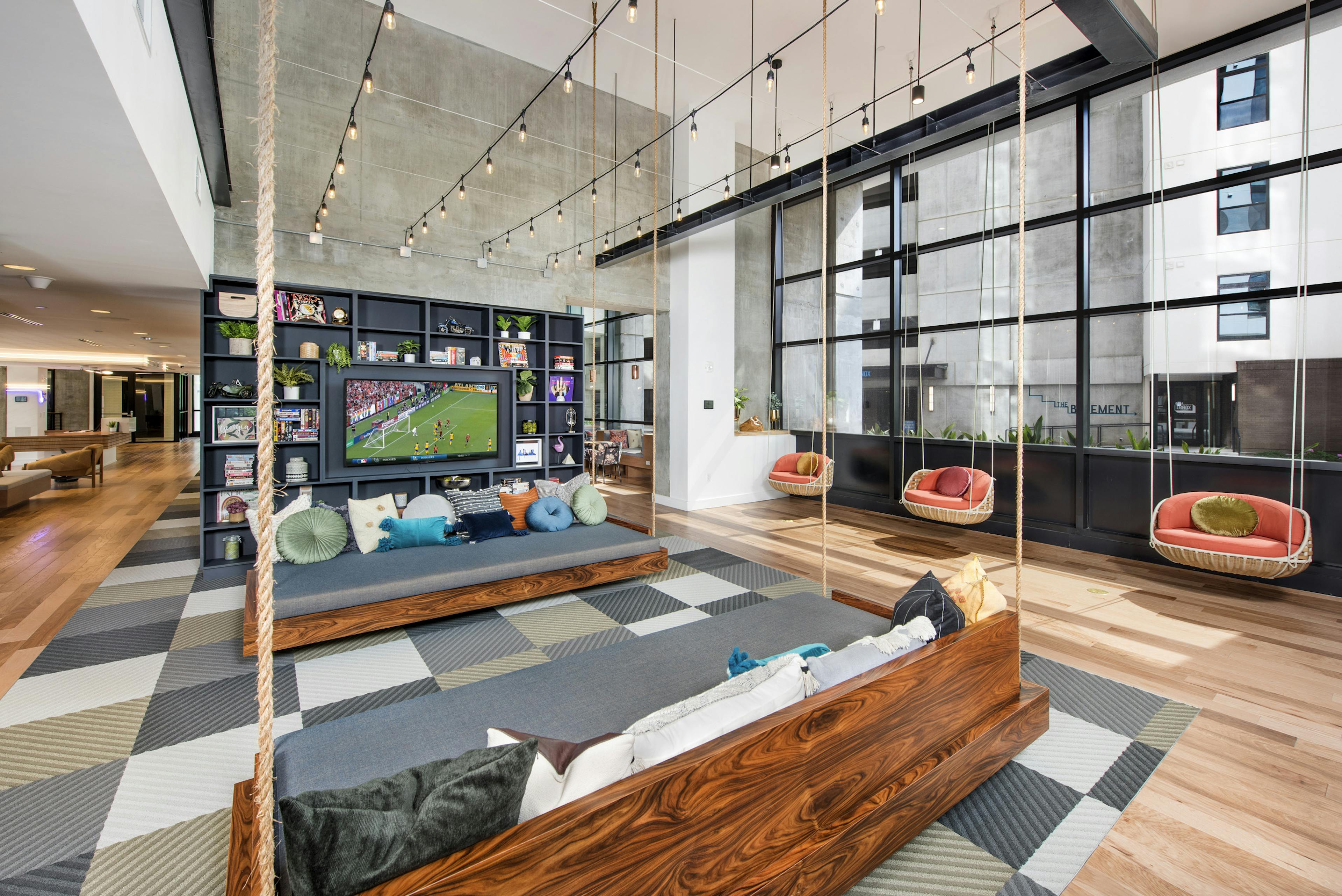 Interior view of AMLI Lenox clubhouse with three swings and seating with lots of colorful pillows and a flat screen TV 
