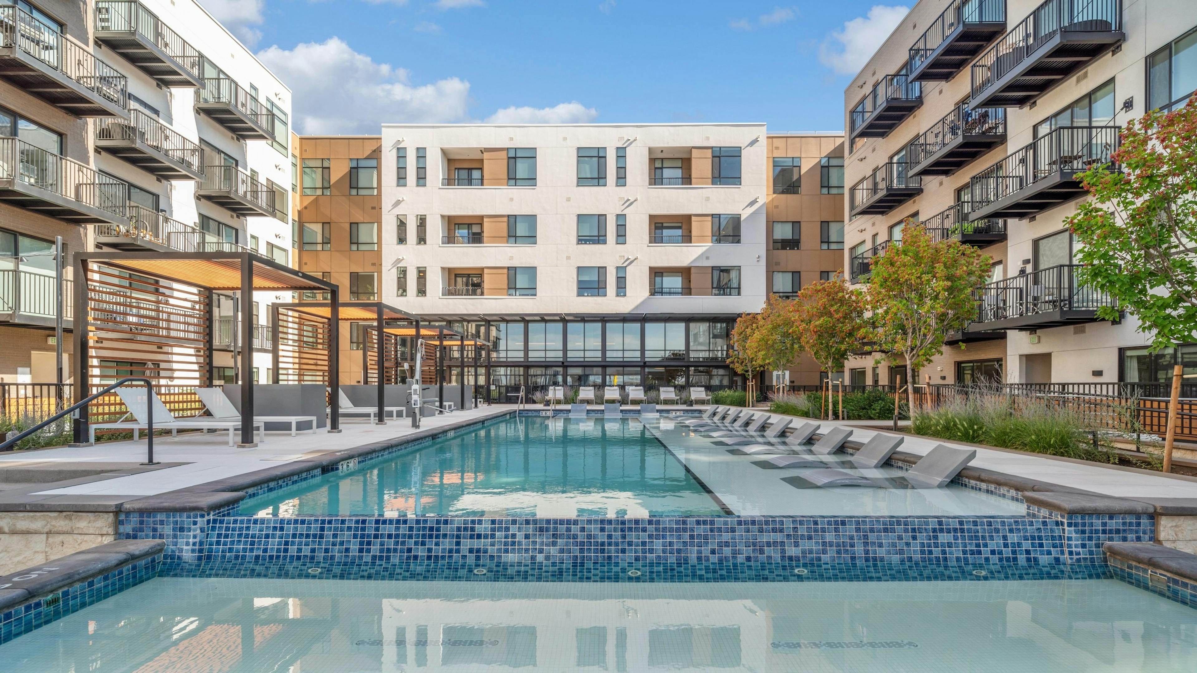 Courtyard pool at AMLI Broadway Park with lounge chairs and cabanas with black metal rail fence surrounded by building  