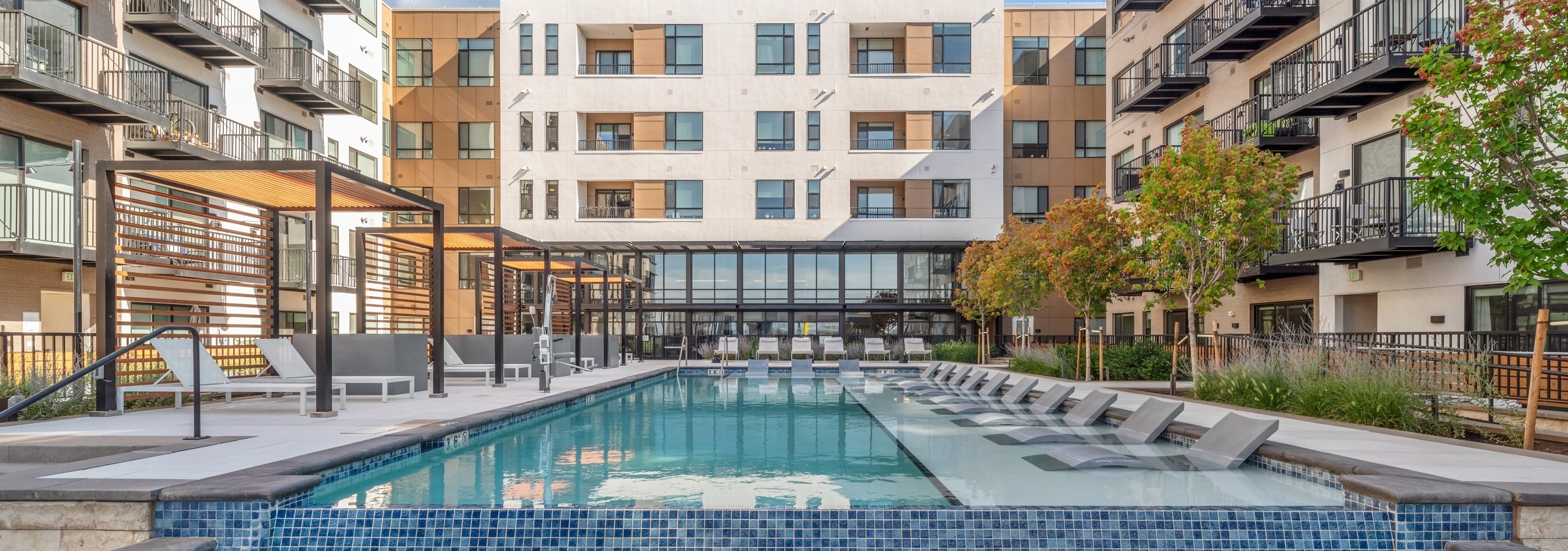 Courtyard pool at AMLI Broadway Park with lounge chairs and cabanas with black metal rail fence surrounded by building