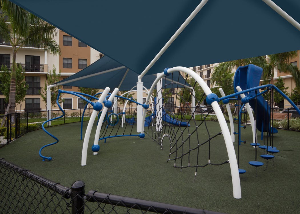 Exterior view of fully covered and gated paw park at AMLI Dadeland with agility equipment surrounded by a grassy run