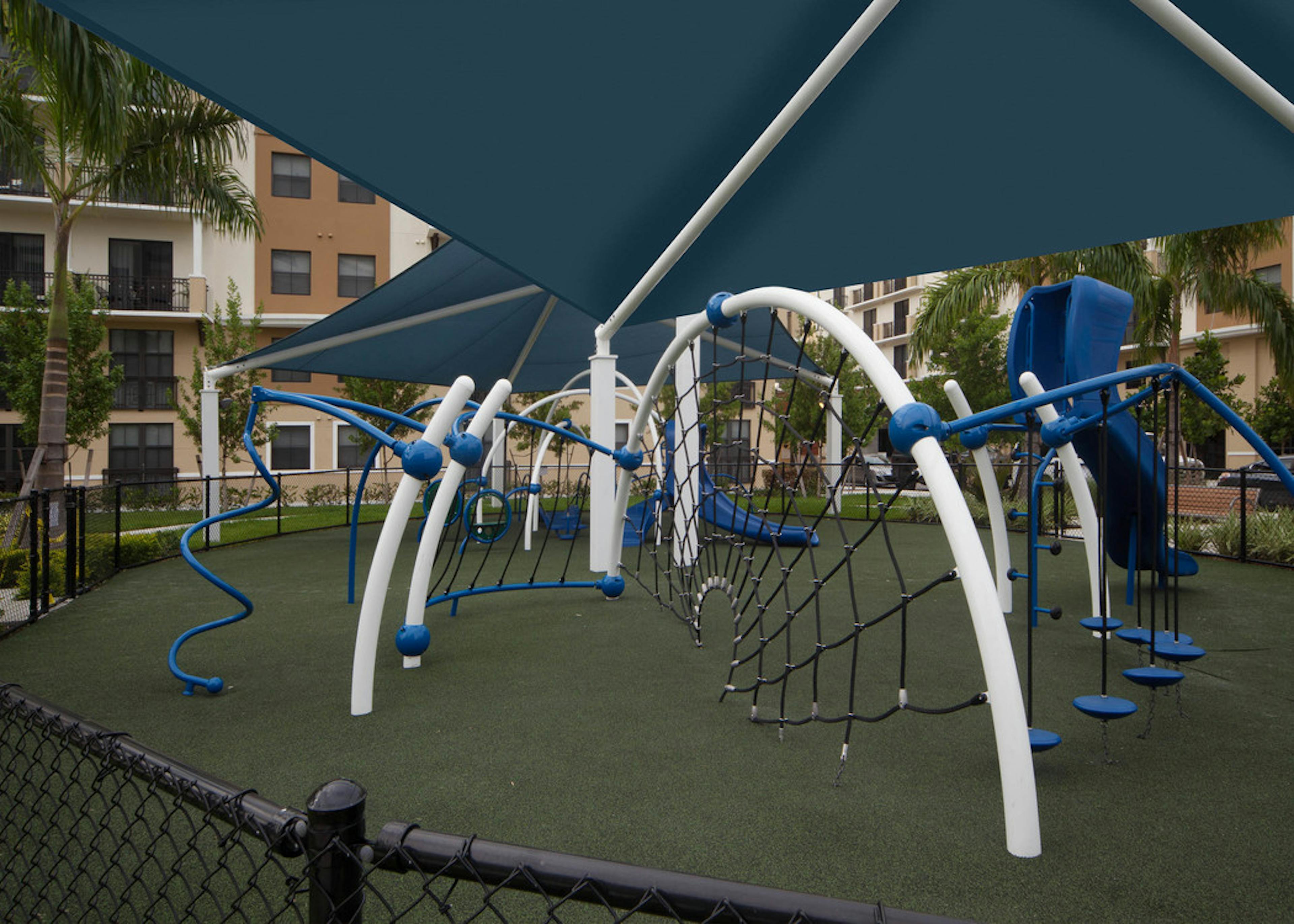 Exterior view of fully covered and gated paw park at AMLI Dadeland with agility equipment surrounded by a grassy run