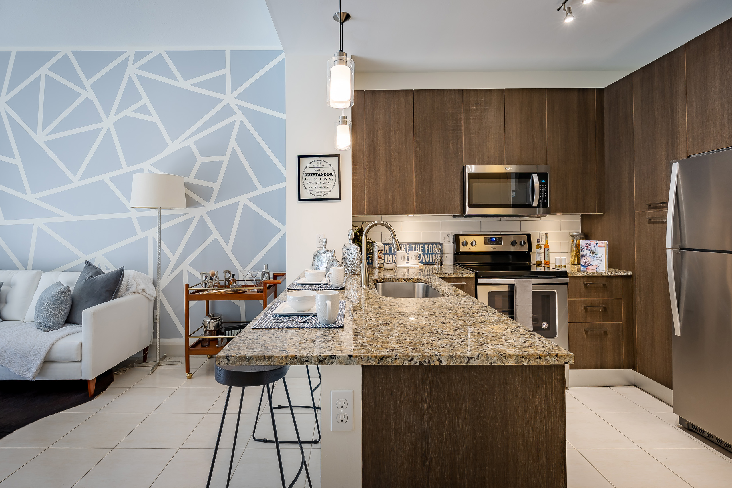 AMLI 8800 apartment kitchen with dark wood cabinets and granite countertop island and stainless steel appliances and living room with blue mosaic wall 