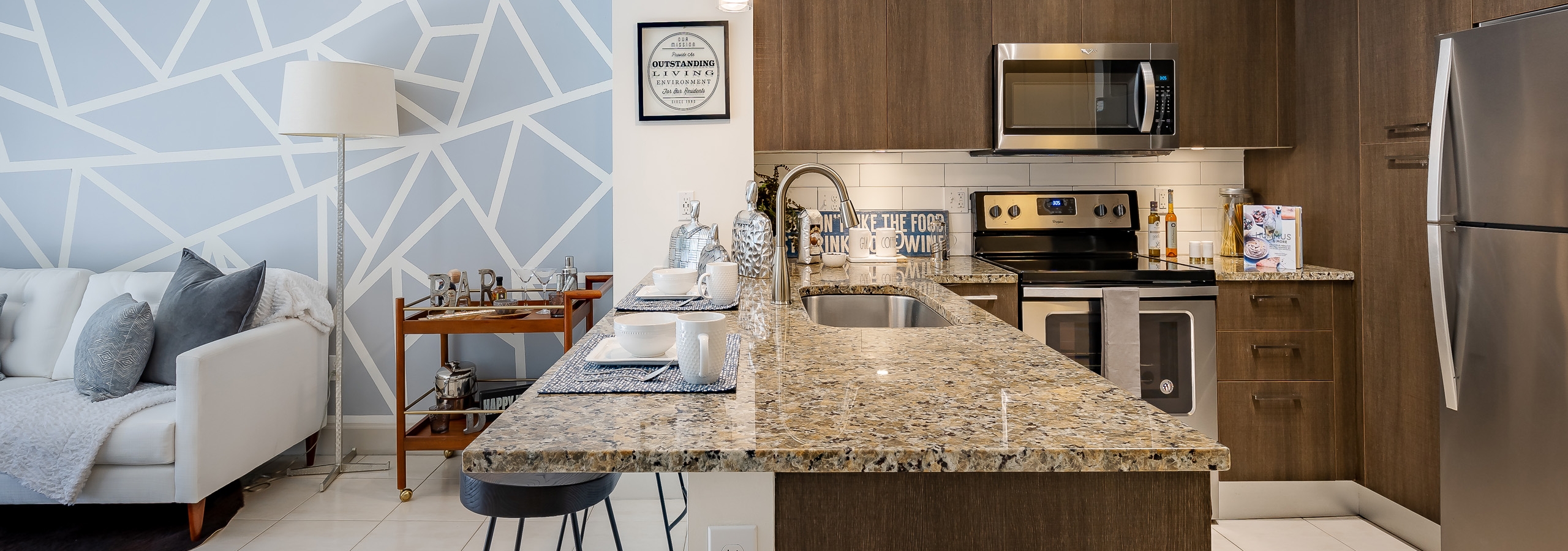 AMLI 8800 apartment kitchen with dark wood cabinets and granite countertop island and stainless steel appliances and living room with blue mosaic wall