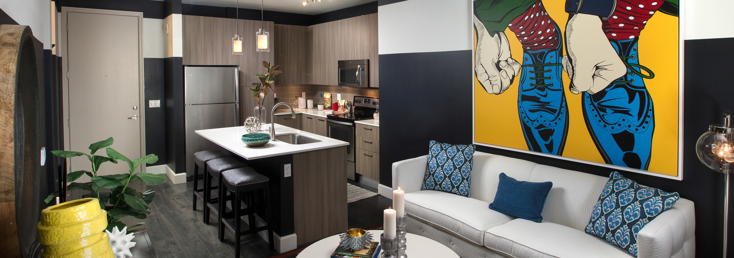 AMLI 8800 apartment living area with white sofa and artwork with blue shoes, toss pillows and a peek into the kitchen