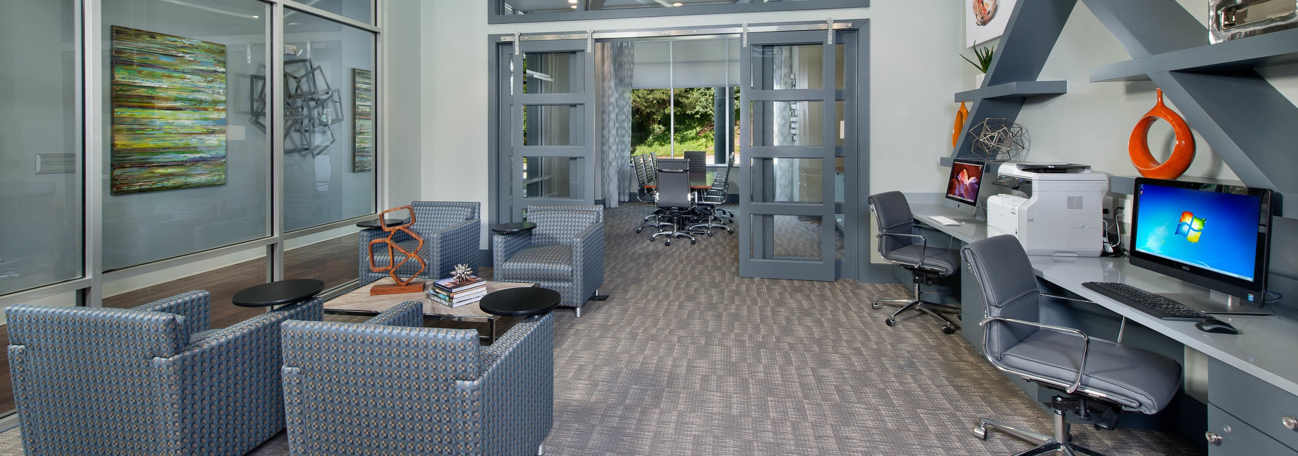 AMLI Piedmont Heights business center showing desk spaces with computers and a printer along with rolling chairs and seating