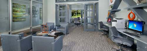AMLI Piedmont Heights business center showing desk spaces with computers and a printer along with rolling chairs and seating