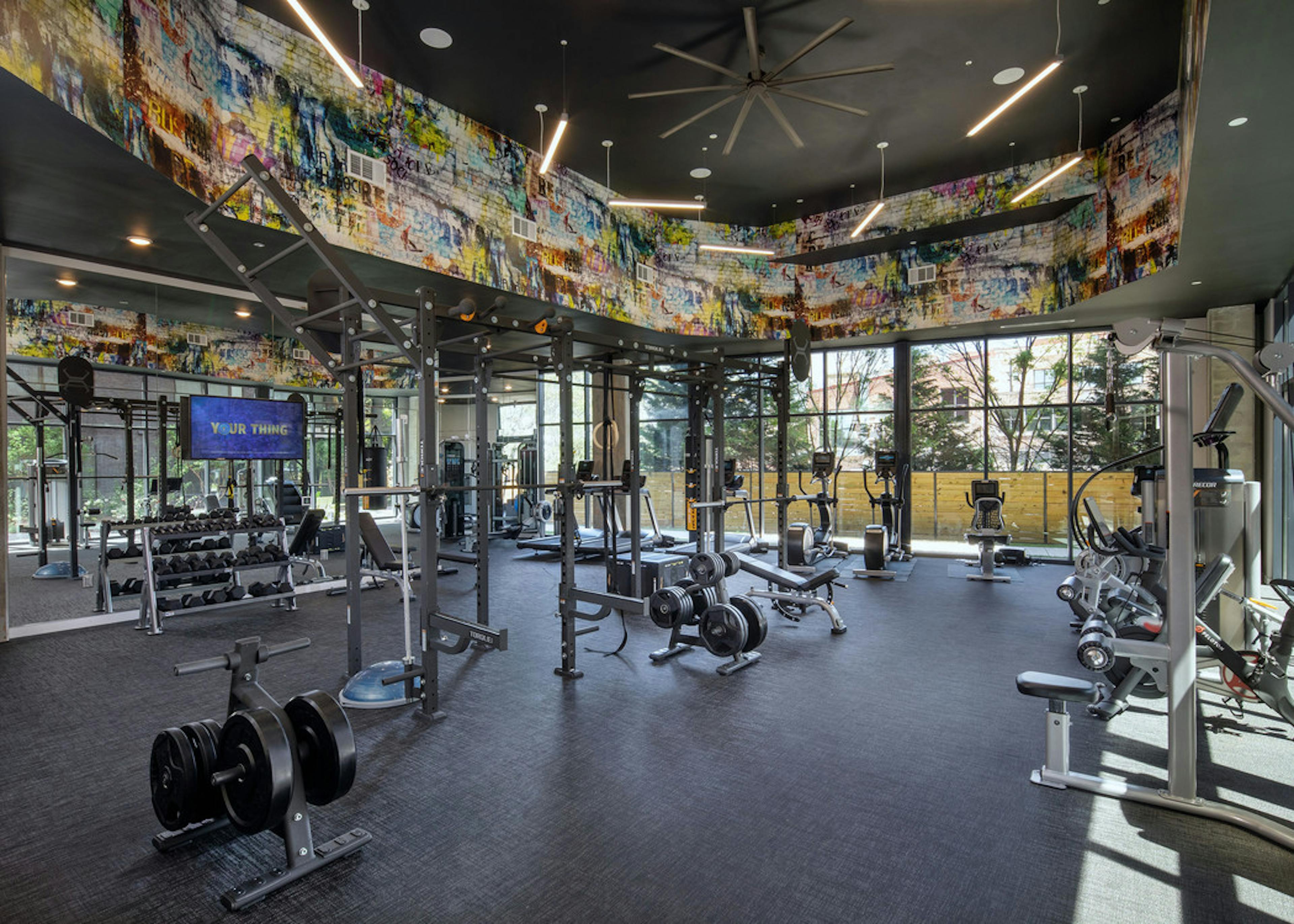 AMLI Westside apartment fitness studio with various weight machines and a free weight station with windows looking outside