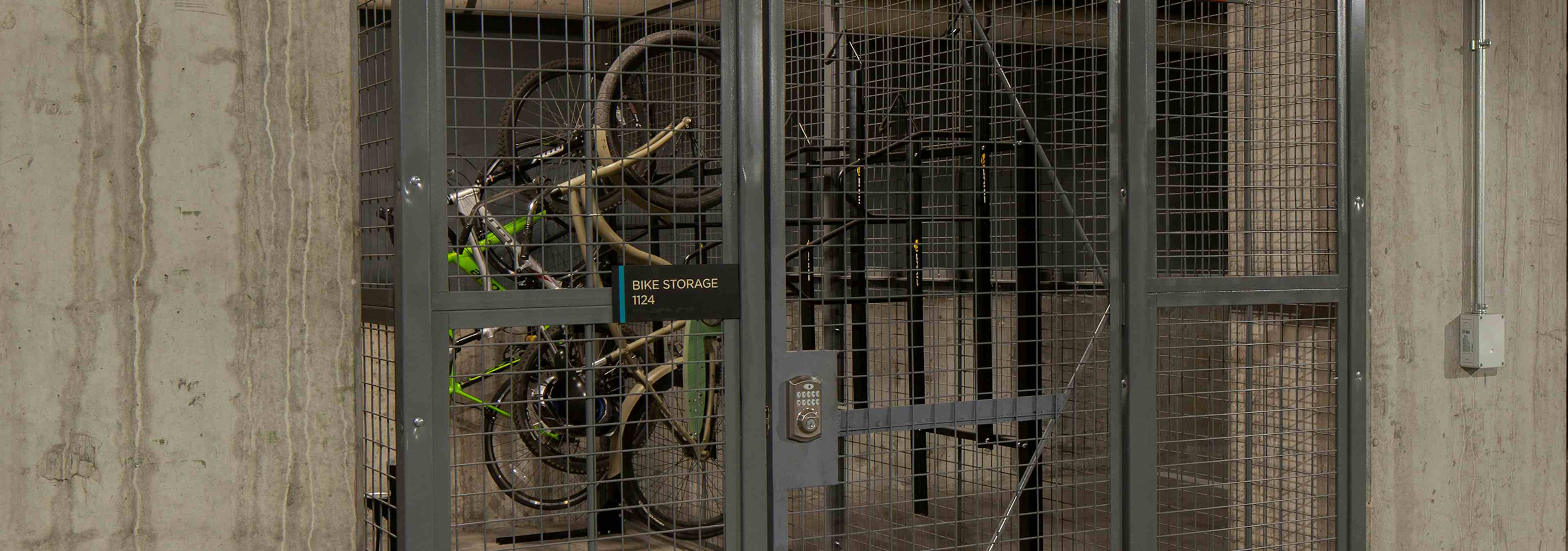 Bike storage cage at AMLI Riverfront Green apartments with metal locked bike cage in parking garage and surrounding cars