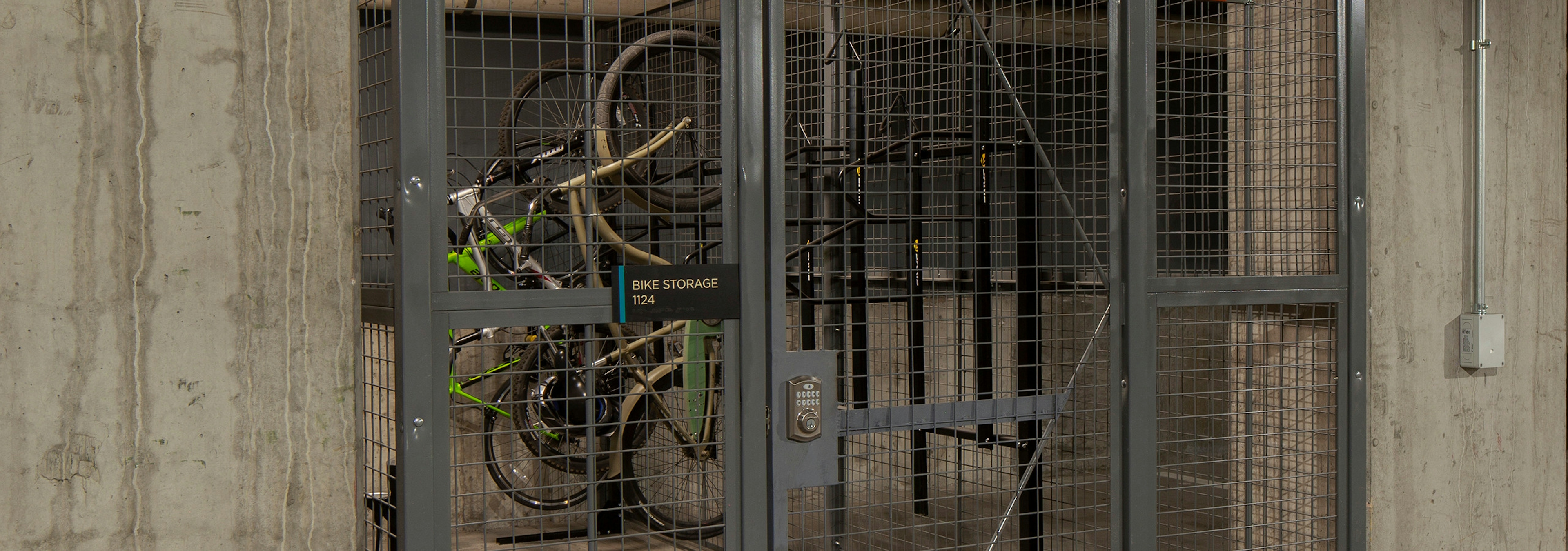 Bike storage cage at AMLI Riverfront Green apartments with metal locked bike cage in parking garage and surrounding cars