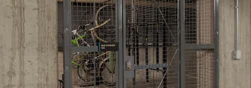 Bike storage cage at AMLI Riverfront Green apartments with metal locked bike cage in parking garage and surrounding cars