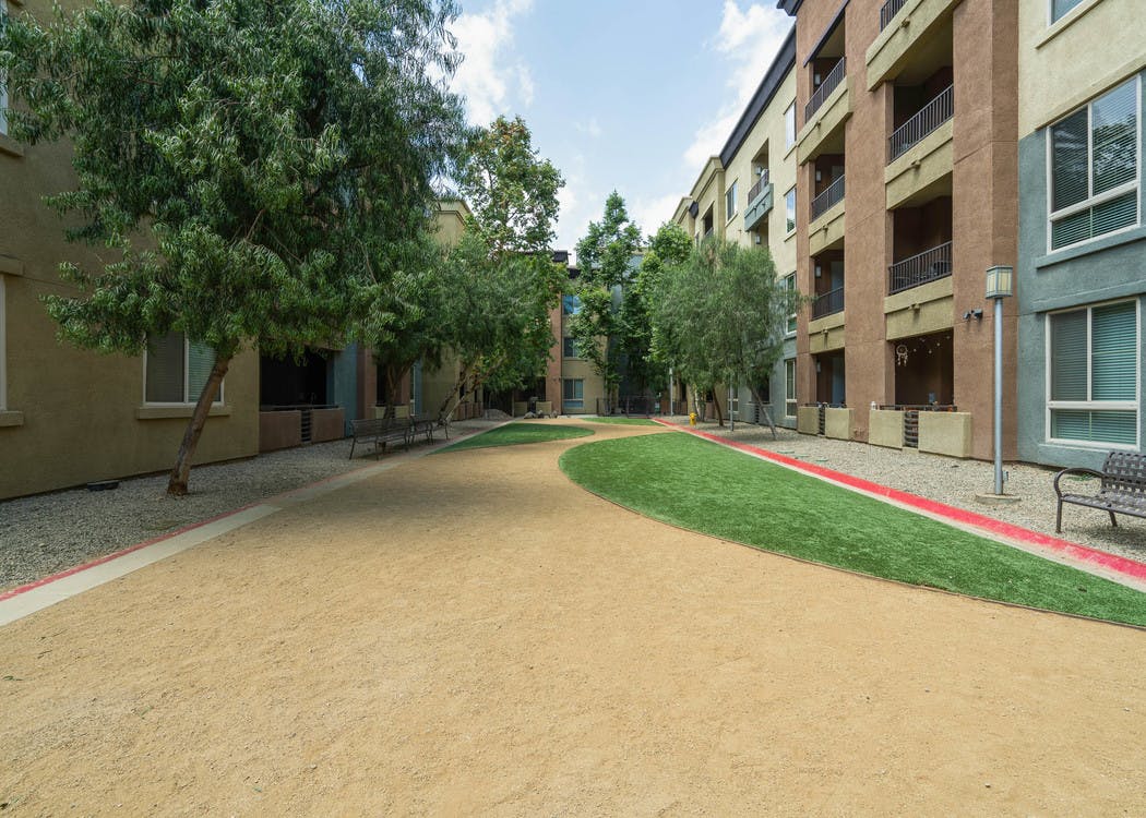 Daytime view of Dog Park with grass, benches and bed of rocks surrounded by trees at AMLI Warner Center apartment building