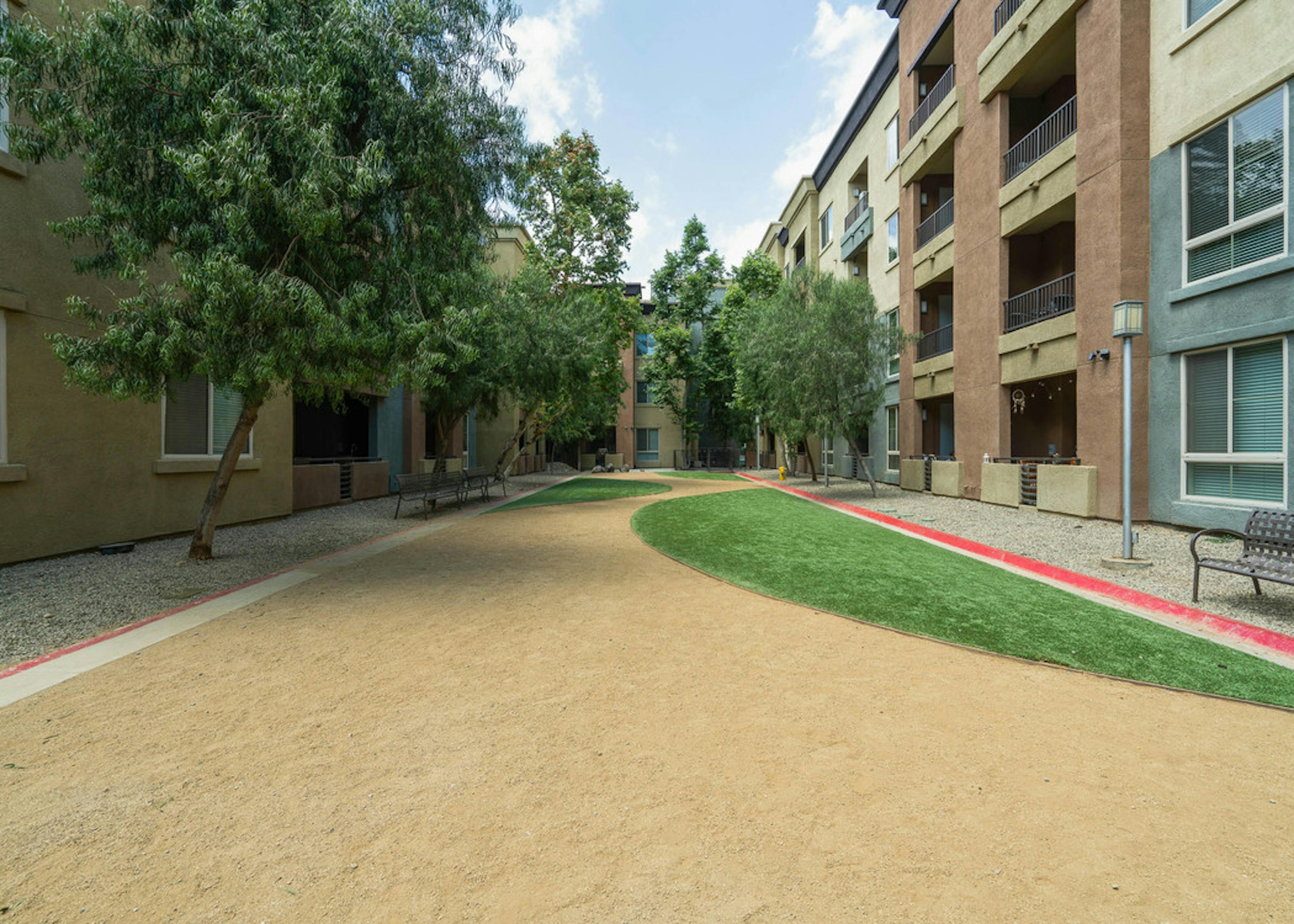 Daytime view of Dog Park with grass, benches and bed of rocks surrounded by trees at AMLI Warner Center apartment building
