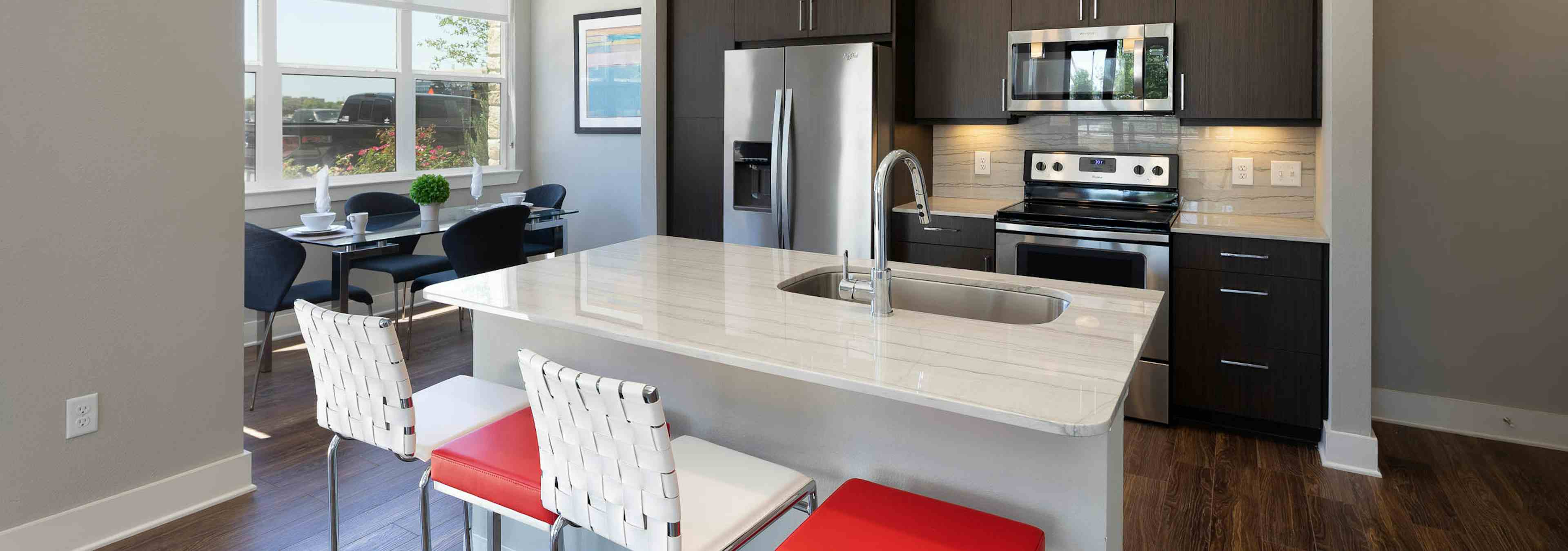 AMLI on Aldrich kitchen with white and red barstools at a quartz island with windows and dark wood cabinetry in background