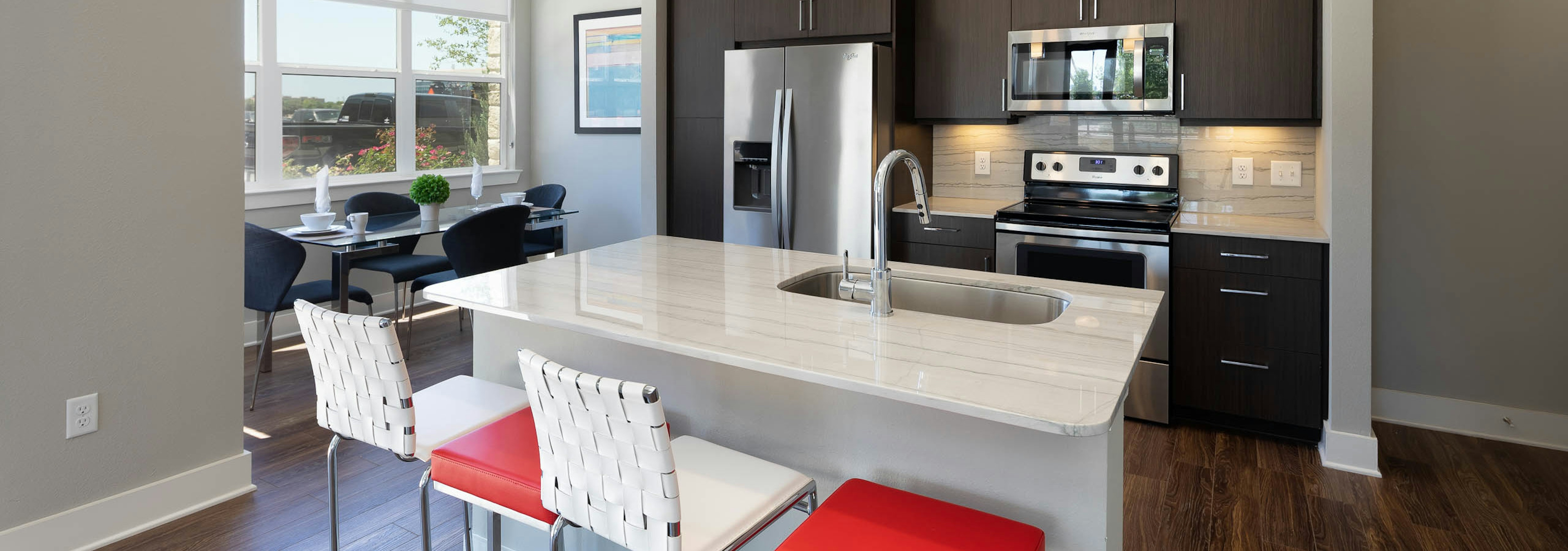 AMLI on Aldrich kitchen with white and red barstools at a quartz island with windows and dark wood cabinetry in background