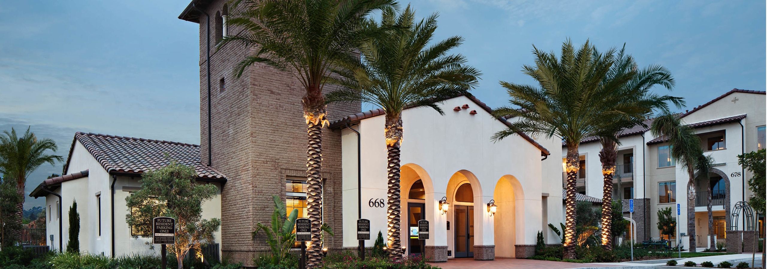 Exterior dusk rendering of AMLI Spanish HIlls apartment building's brick facade with arched entrance to office and palm trees