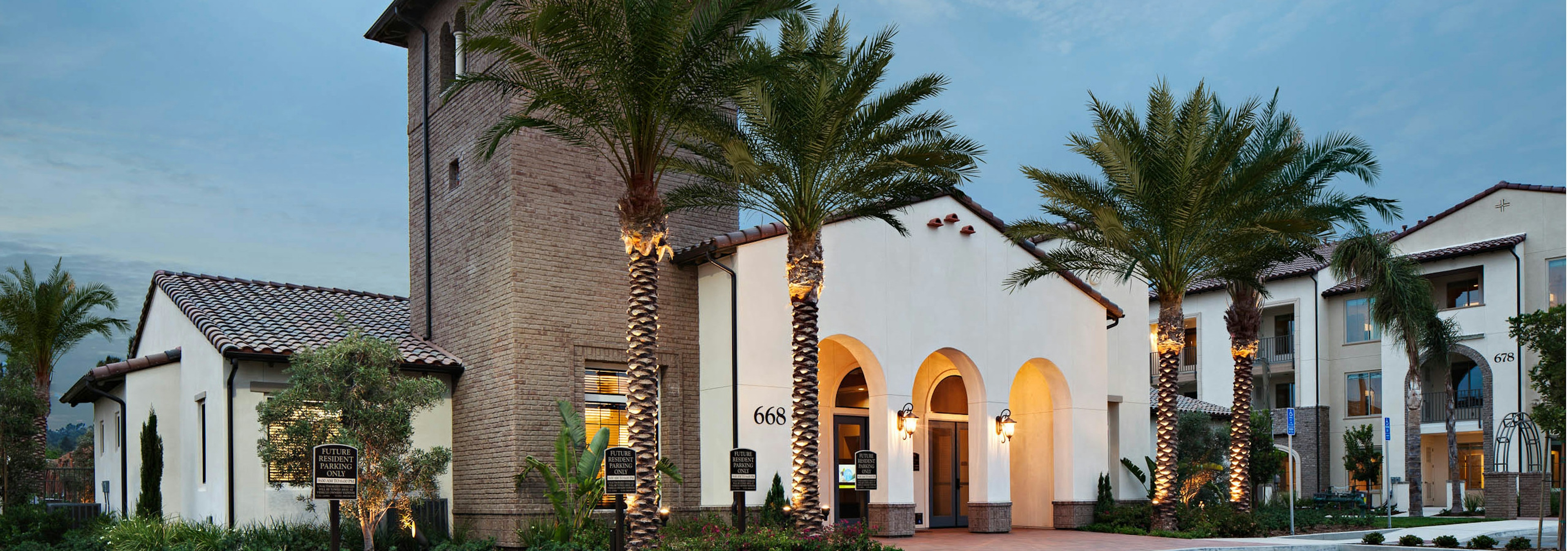 Exterior dusk rendering of AMLI Spanish HIlls apartment building's brick facade with arched entrance to office and palm trees