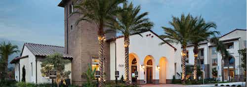 Exterior dusk rendering of AMLI Spanish HIlls apartment building's brick facade with arched entrance to office and palm trees