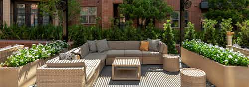 Daytime view of resident cabana area with a large wicker L shaped couch and table surrounded by lush greenery and flowers