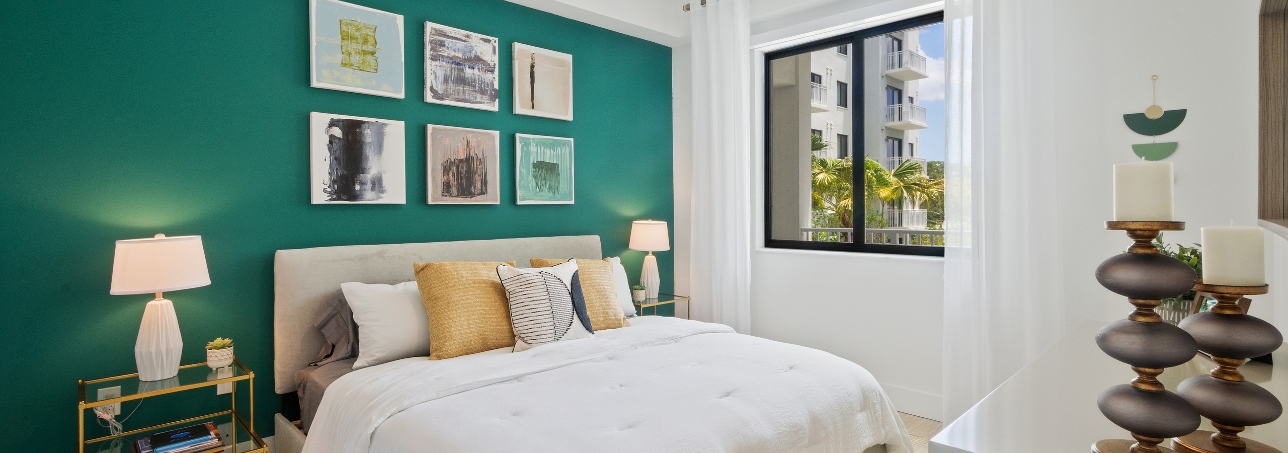 AMLI Park West apartment bedroom with queen bed on teal wall with two gold nightstands and white lamps and side window