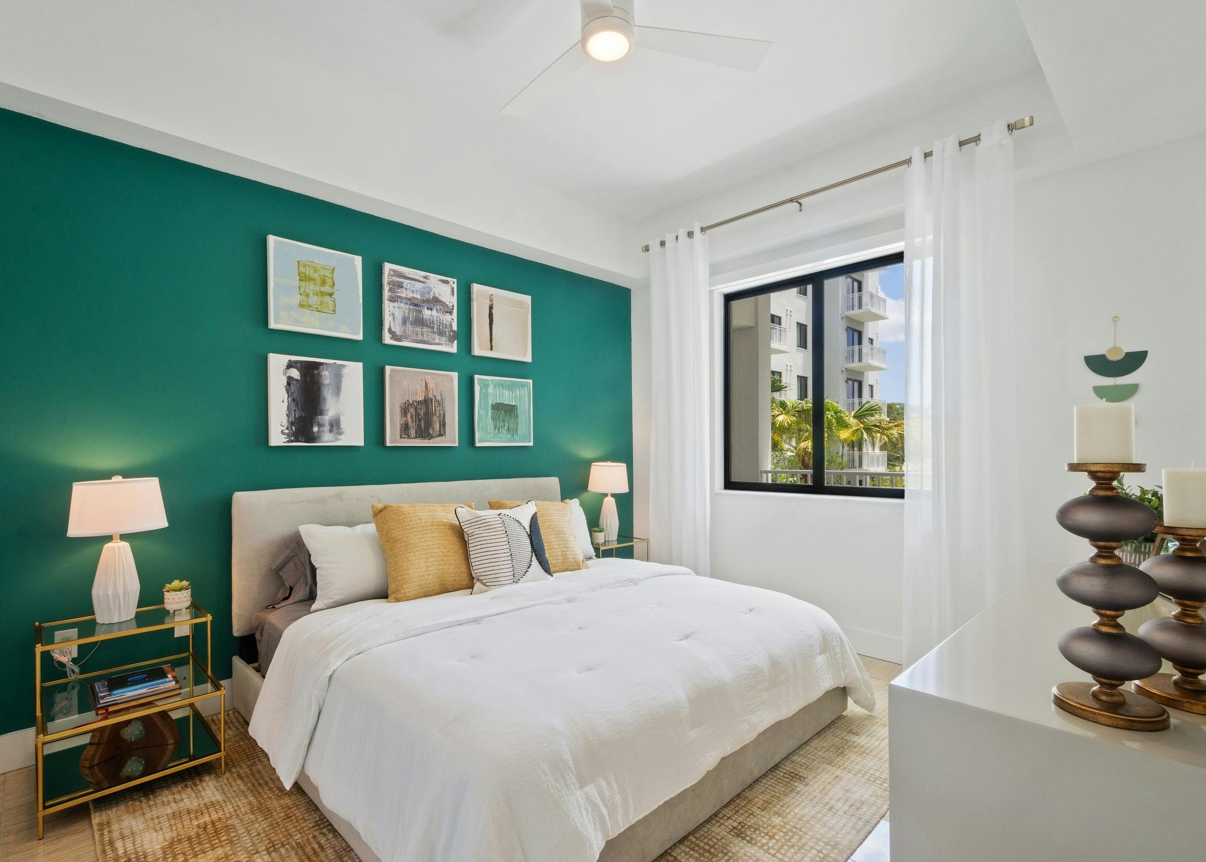 AMLI Park West apartment bedroom with queen bed on teal wall with two gold nightstands and white lamps and side window