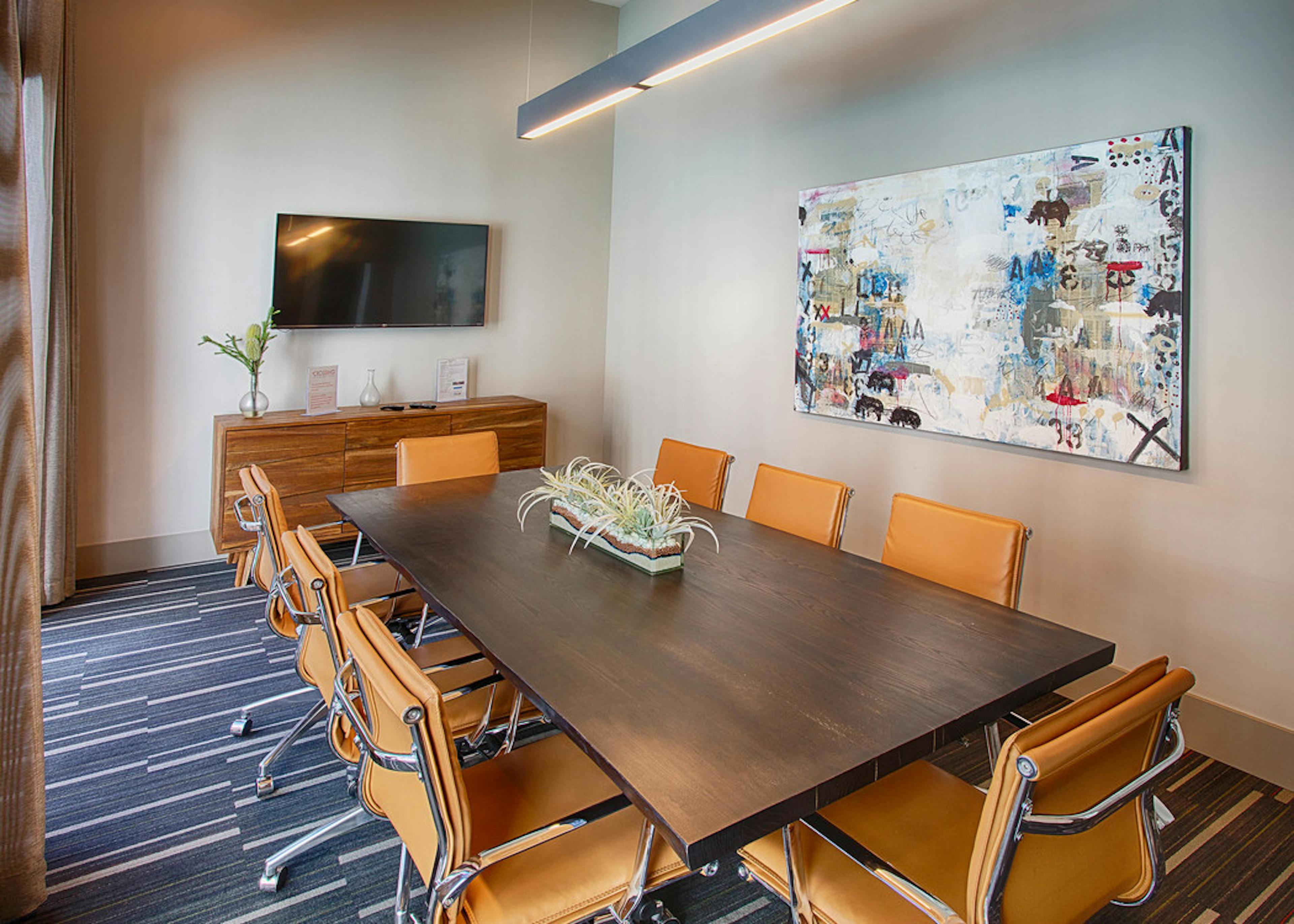 A conference room at AMLI Denargo Market apartments with a long table and chairs and a large piece of art and television 