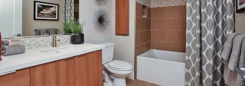 Interior view of AMLI Uptown Orange apartment bathroom with quartz countertop and large soaking tub with tile surround