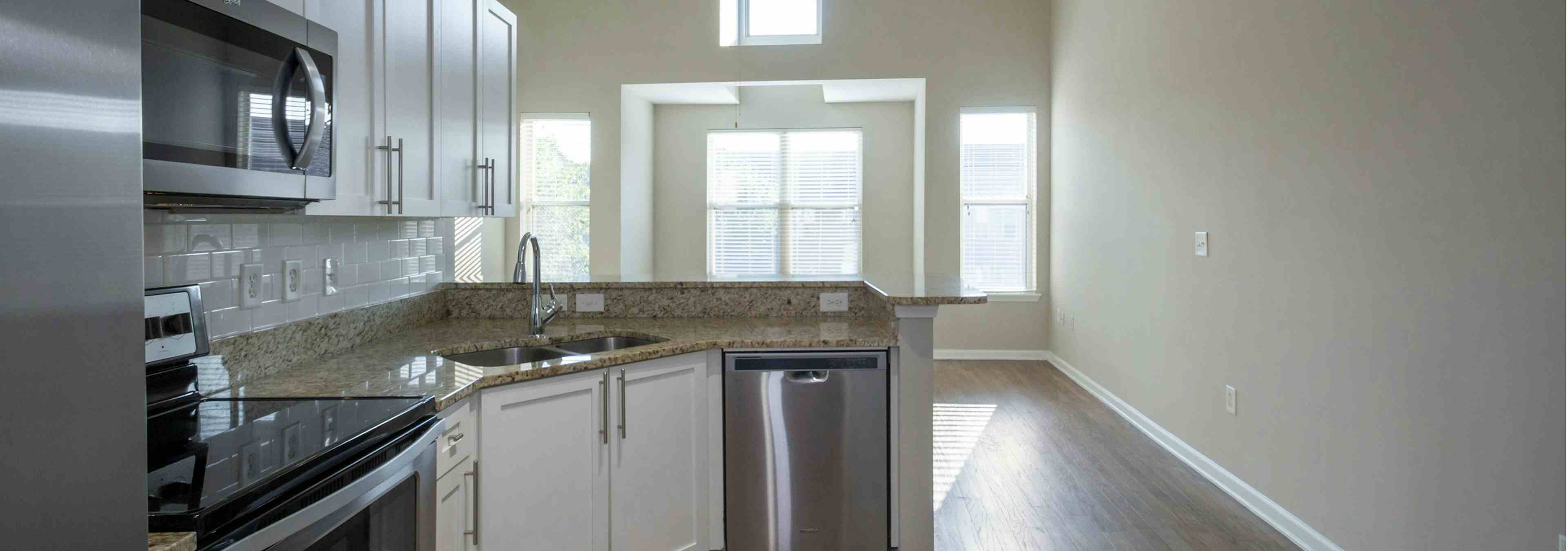 Interior view of AMLI Lindbergh apartment kitchen with white cabinets, granite countertops, and stainless steel appliances