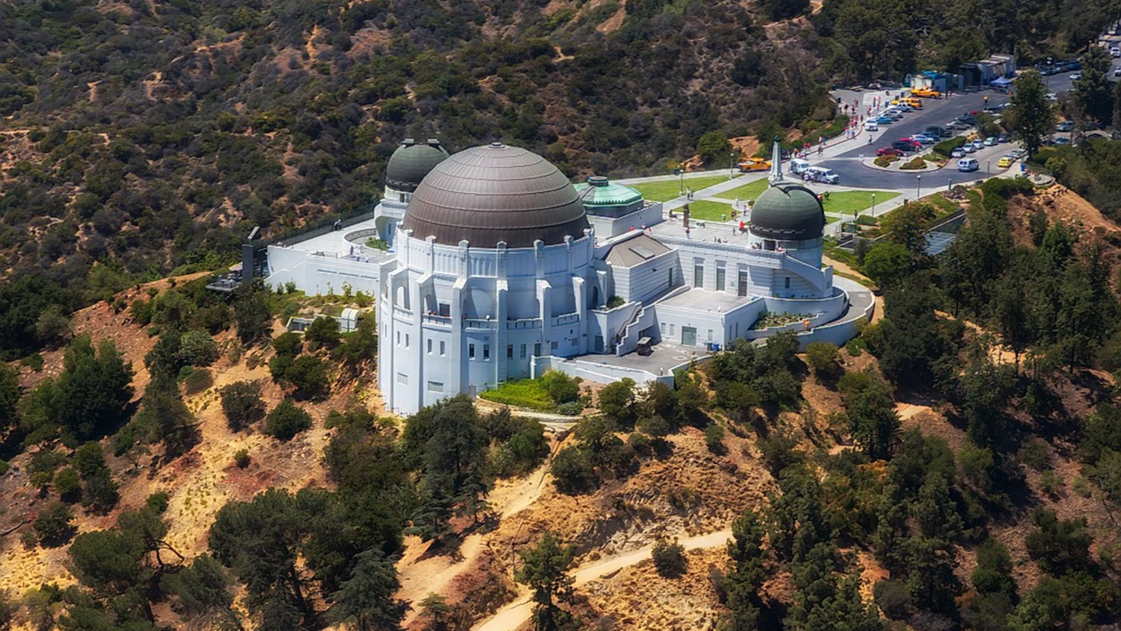 The Griffith Observatory from afar on a sunbathed hill surrounded by shrubs and trees
