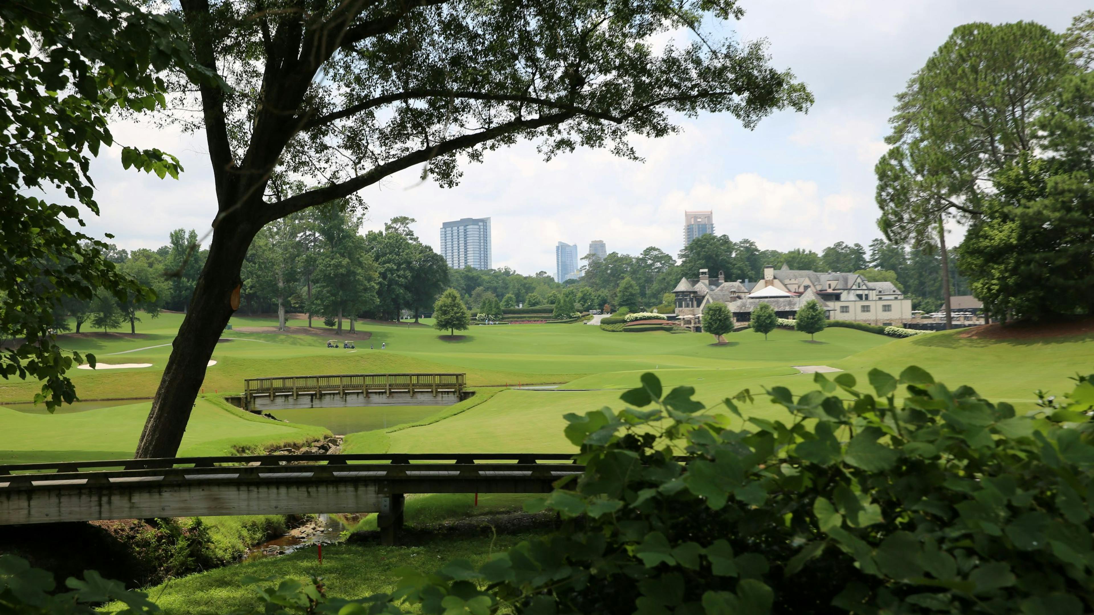 Scenic daytime view of Brookhaven skyline and  golf course and clubhouse from shrubbery behind a bridge