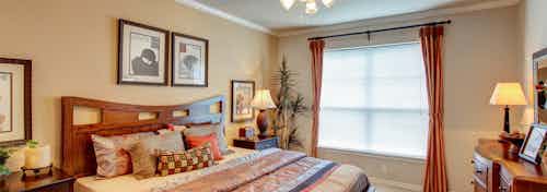 Interior of AMLI Memorial Heights apartment bedroom with bed, nightstands, dresser and large window with blinds and curtains