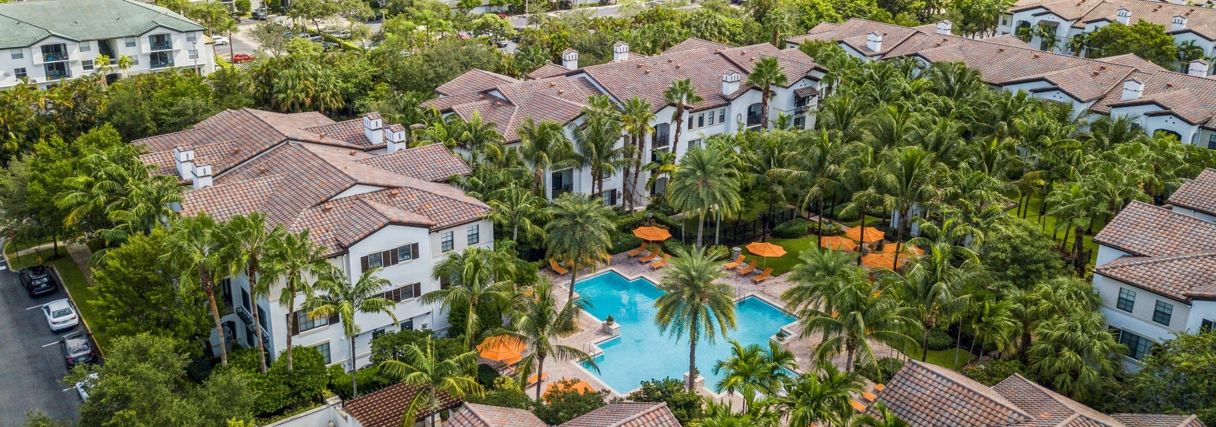 Aerial photo of AMLI Toscana Place apartments with pool surrounded by orange umbrellas and palm trees and white buildings