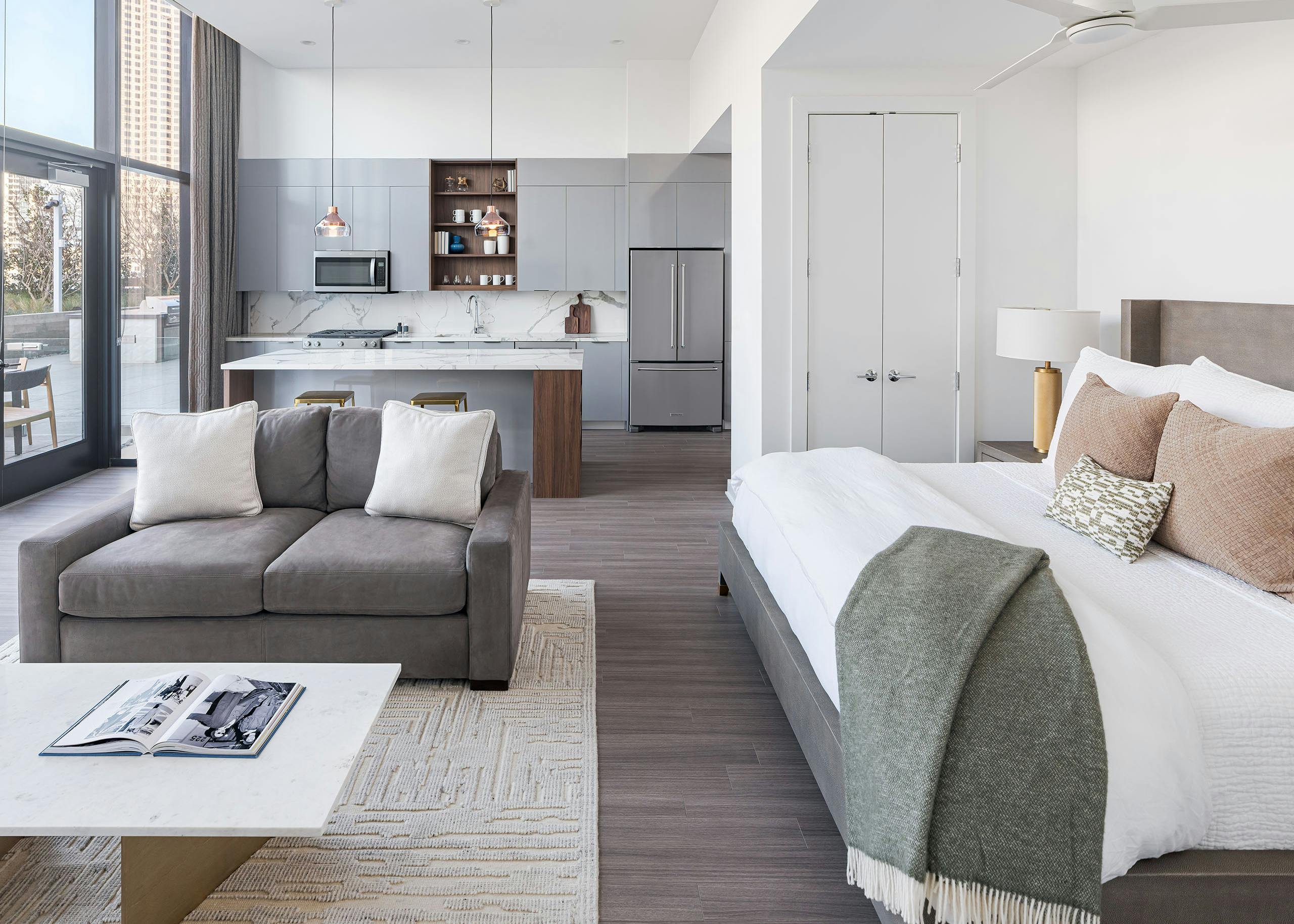 AMLI Fountain Place studio apartment with large white bed and grey couch with white coffee table and grey island kitchen