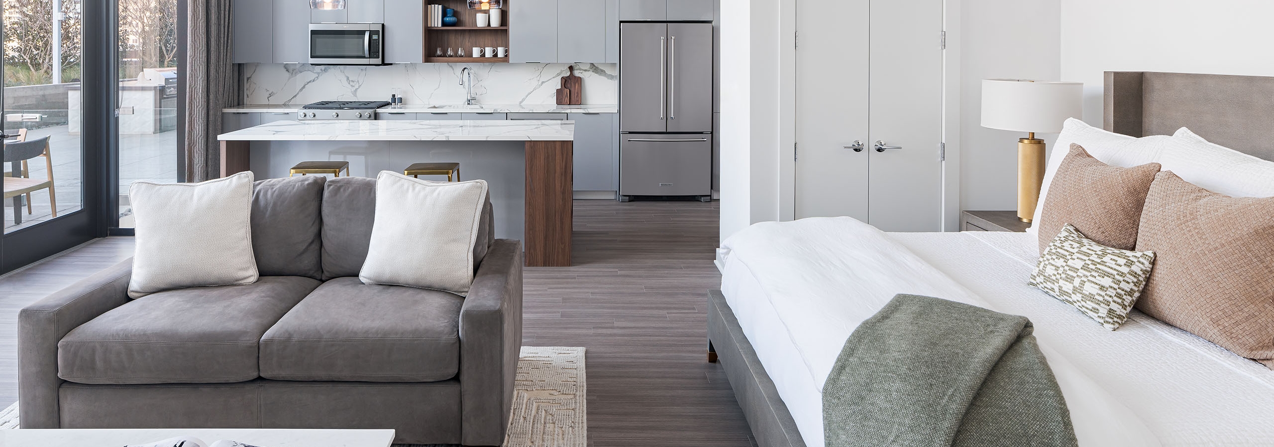 AMLI Fountain Place studio apartment with large white bed and grey couch with white coffee table and grey island kitchen