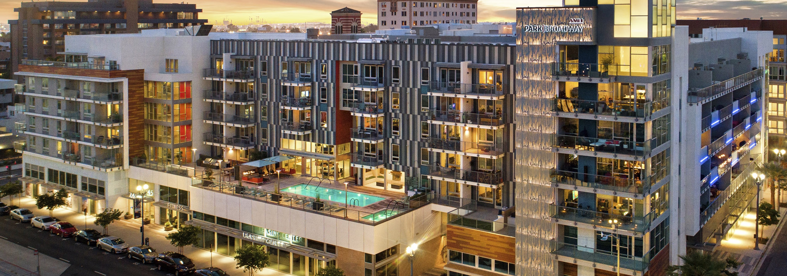 Aerial dusk exterior view of AMLI Park Broadway apartment building with lit rooftop pool and tree lined street below