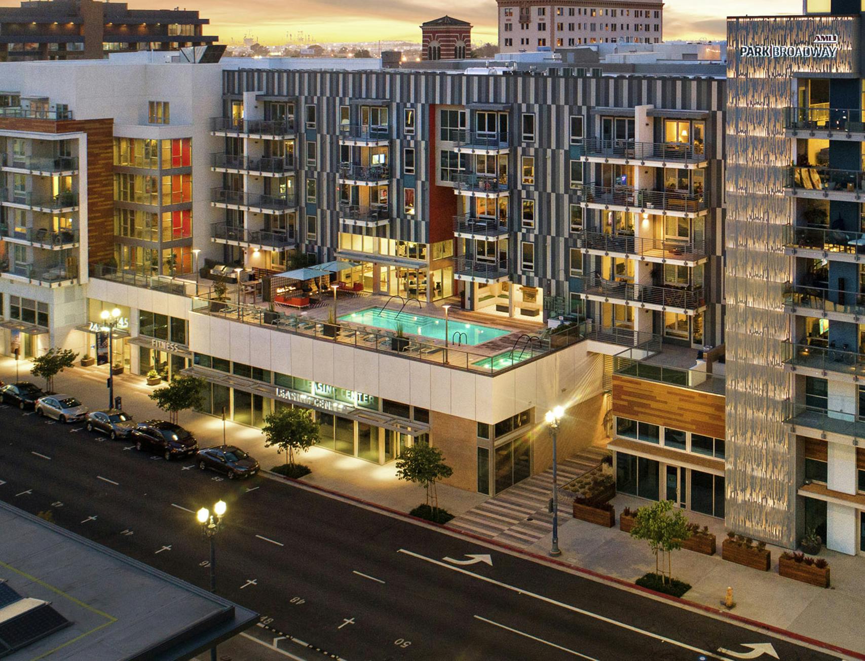 Aerial dusk exterior view of AMLI Park Broadway apartment building with lit rooftop pool and tree lined street below