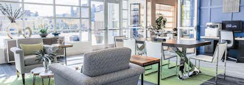 A cyber cafe at AMLI Arista apartments with plush chairs and a table with chairs and a computer as well as windows and a door