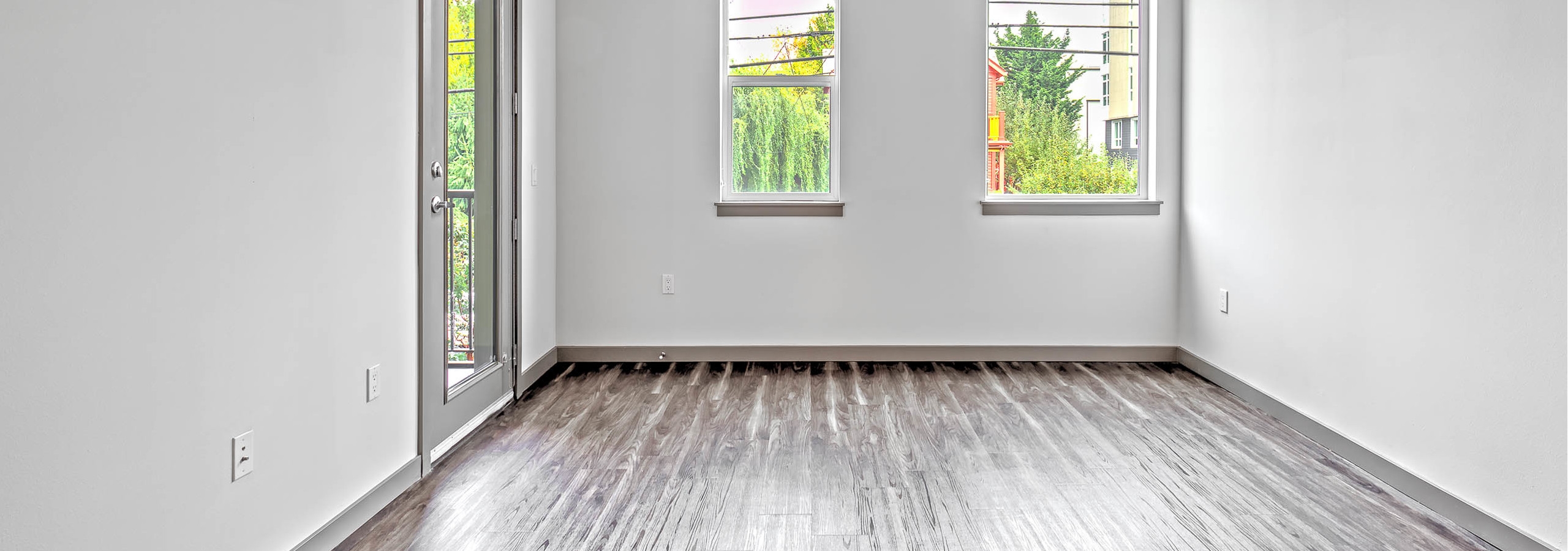 Interior view of AMLI Mark24 living room with laminate floor large windows white walls and door to patio