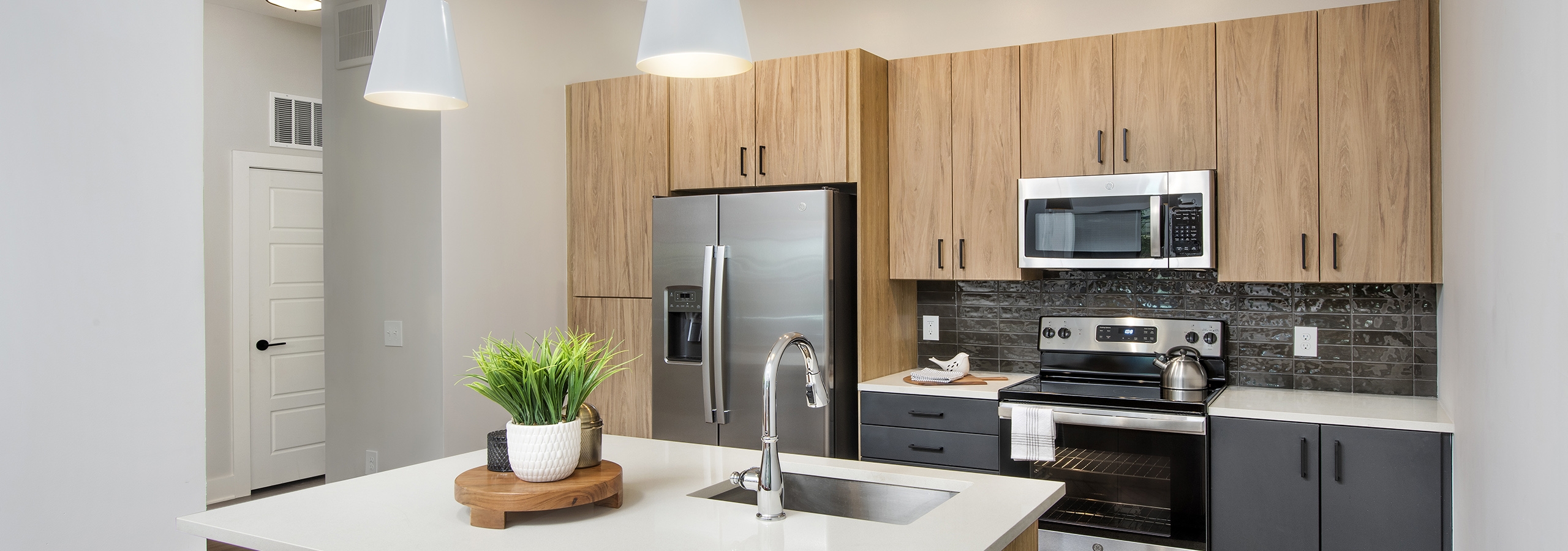 AMLI Flatiron kitchen with light woodgrain cabinets and stainless steel appliances with large white island and orange chairs