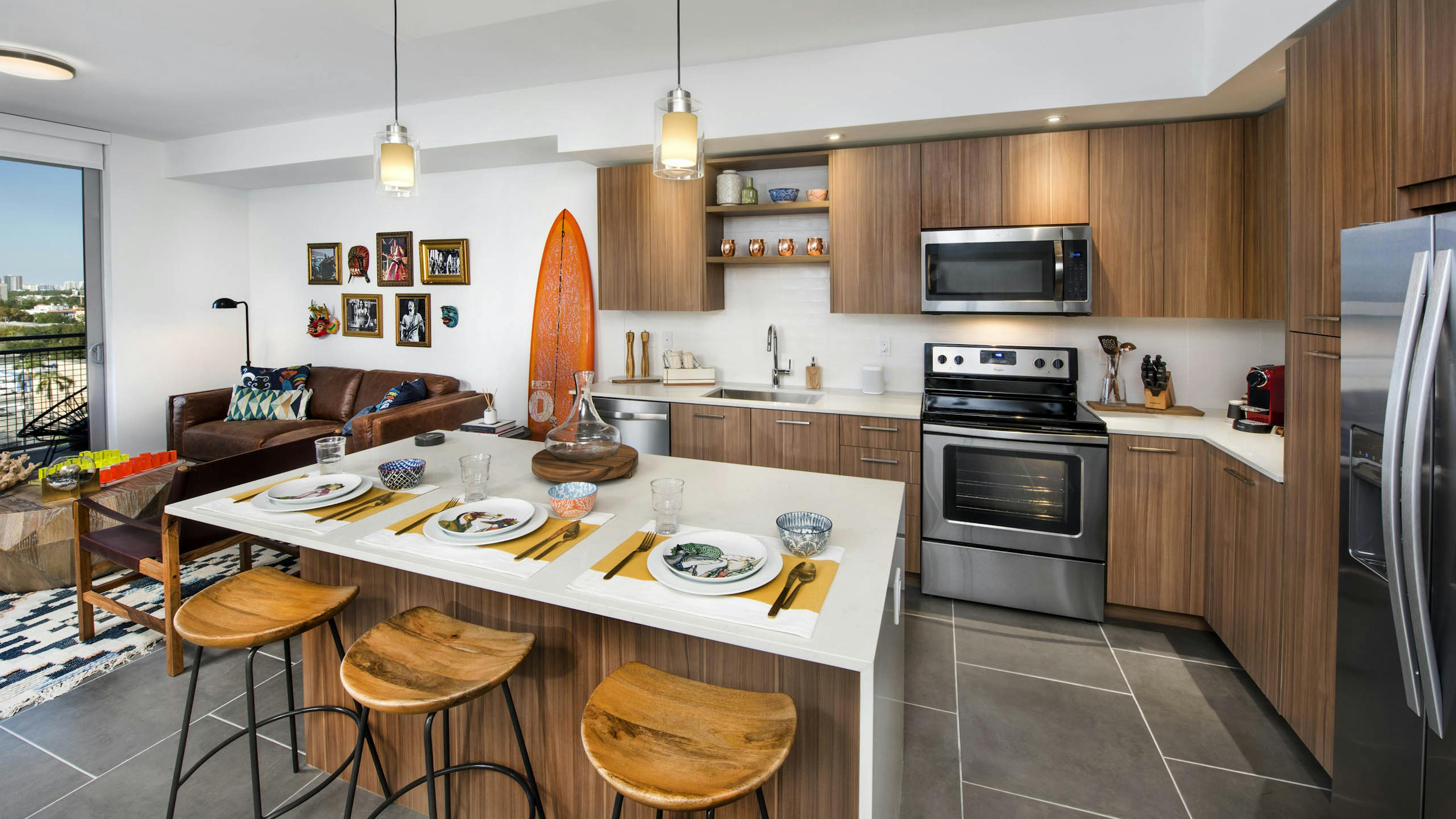 AMLI Midtown 29 kitchen with white island and wood stools and pendant lights and orange surfboard on wall beside wood cabinets
