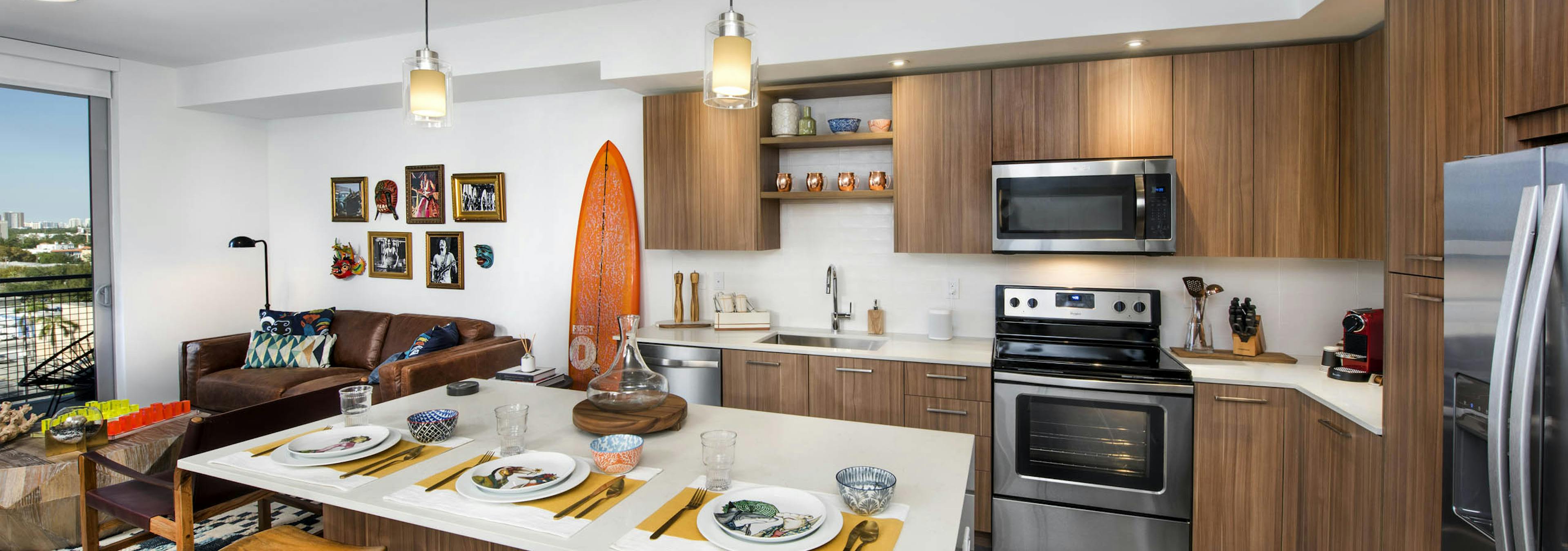 AMLI Midtown 29 kitchen with white island and wood stools and pendant lights and orange surfboard on wall beside wood cabinets
