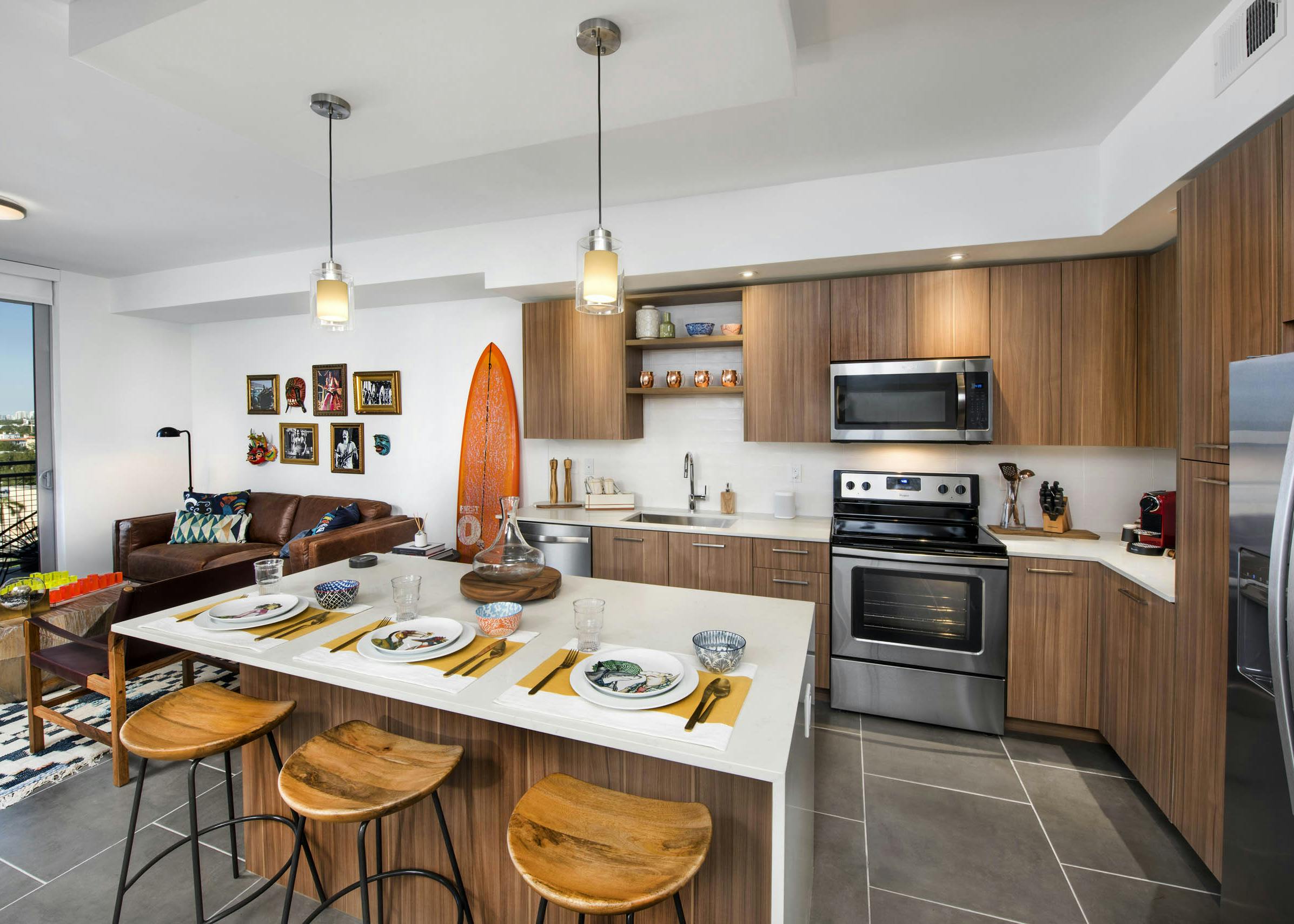 AMLI Midtown 29 kitchen with white island and wood stools and pendant lights and orange surfboard on wall beside wood cabinets