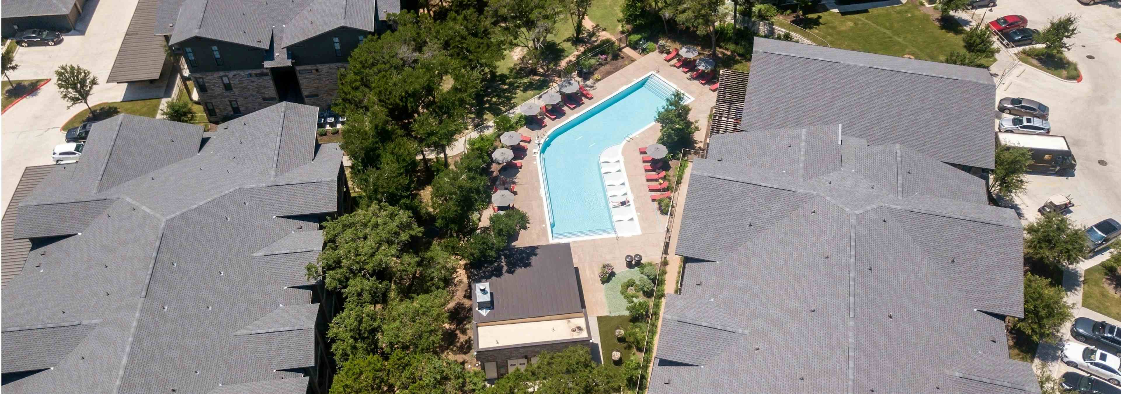 Daytime aerial view of AMLI Covered Bridge community pool with red lounge chairs and grey umbrellas for shade