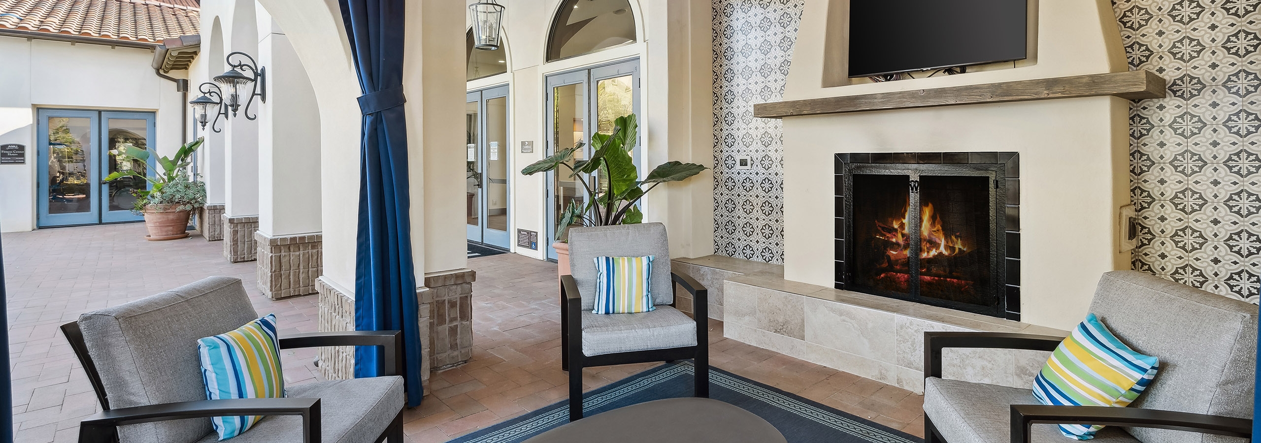 Private nook with big screen TV above the fireplace offering plush lounge seating and hanging lights at AMLI Spanish Hills