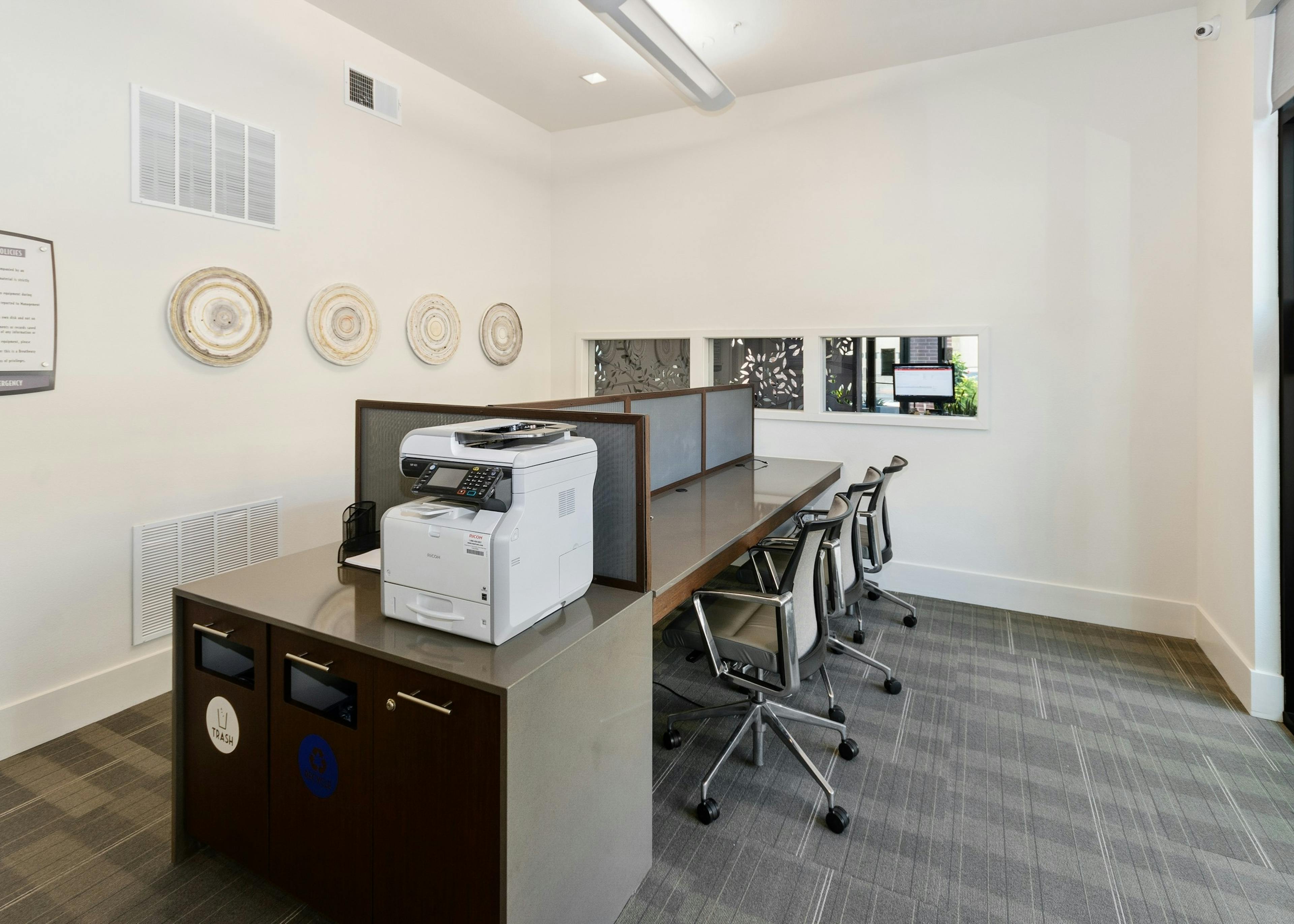AMLI West Plano business center with multiple wooden workstations including metal swivel chairs and art installations on the walls