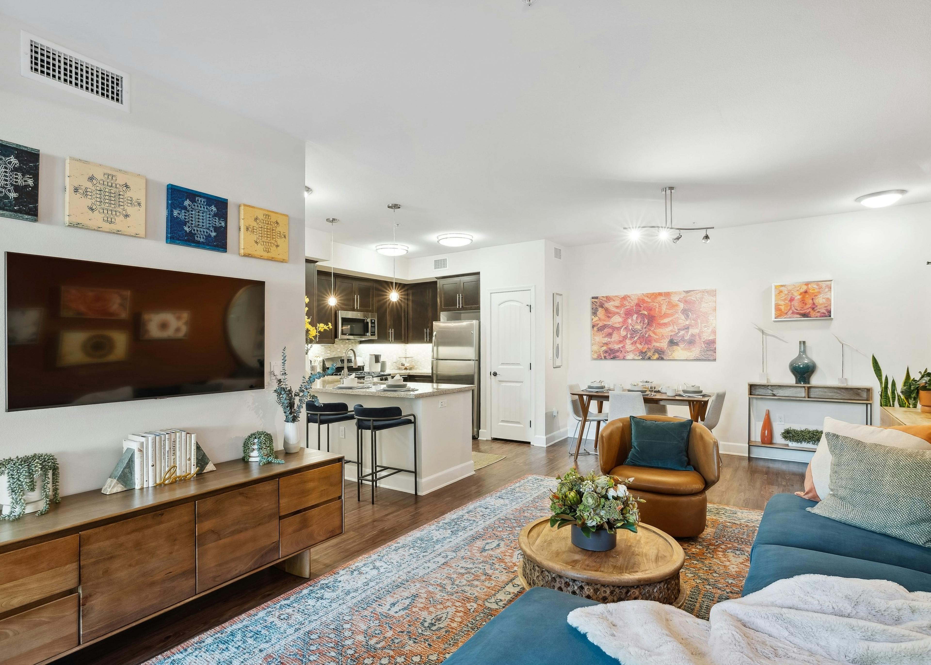 Furnished living room with blue couch and plush pillows and TV and artwork on walls at AMLI Spanish Hills