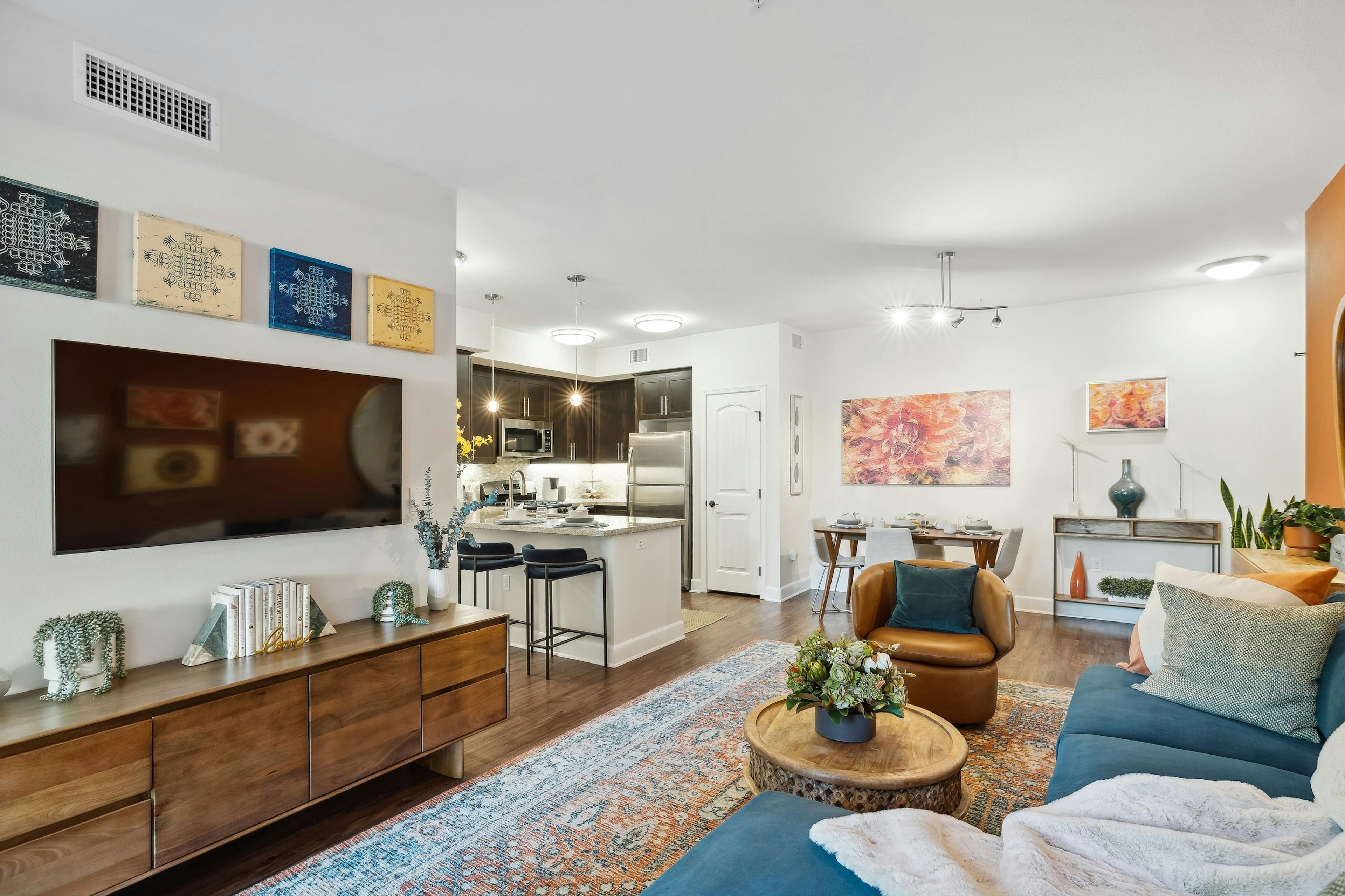 Furnished living room with blue couch and plush pillows and TV and artwork on walls at AMLI Spanish Hills
