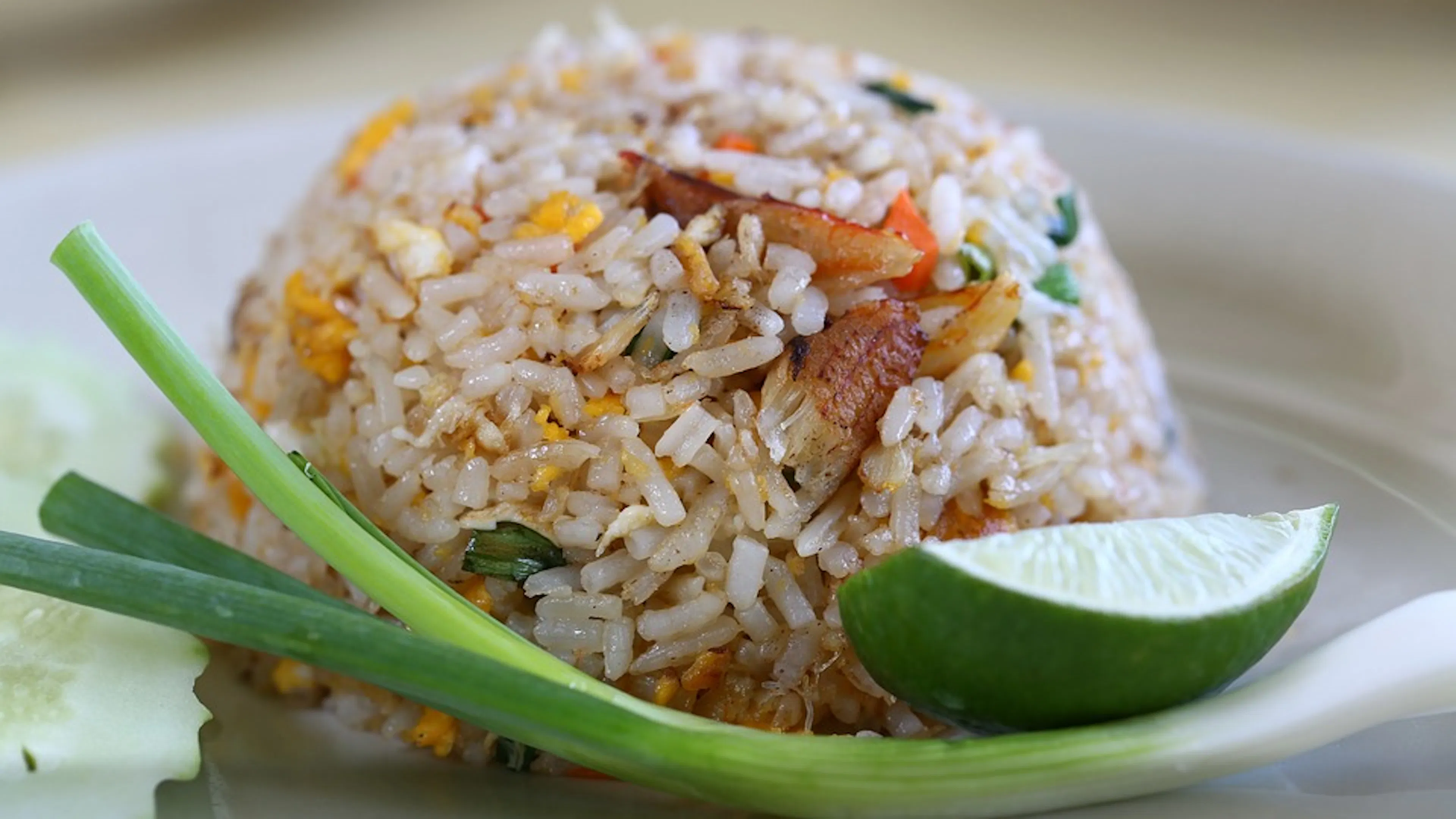 A mound of chicken fried rice next to a green onion and a slice of lime