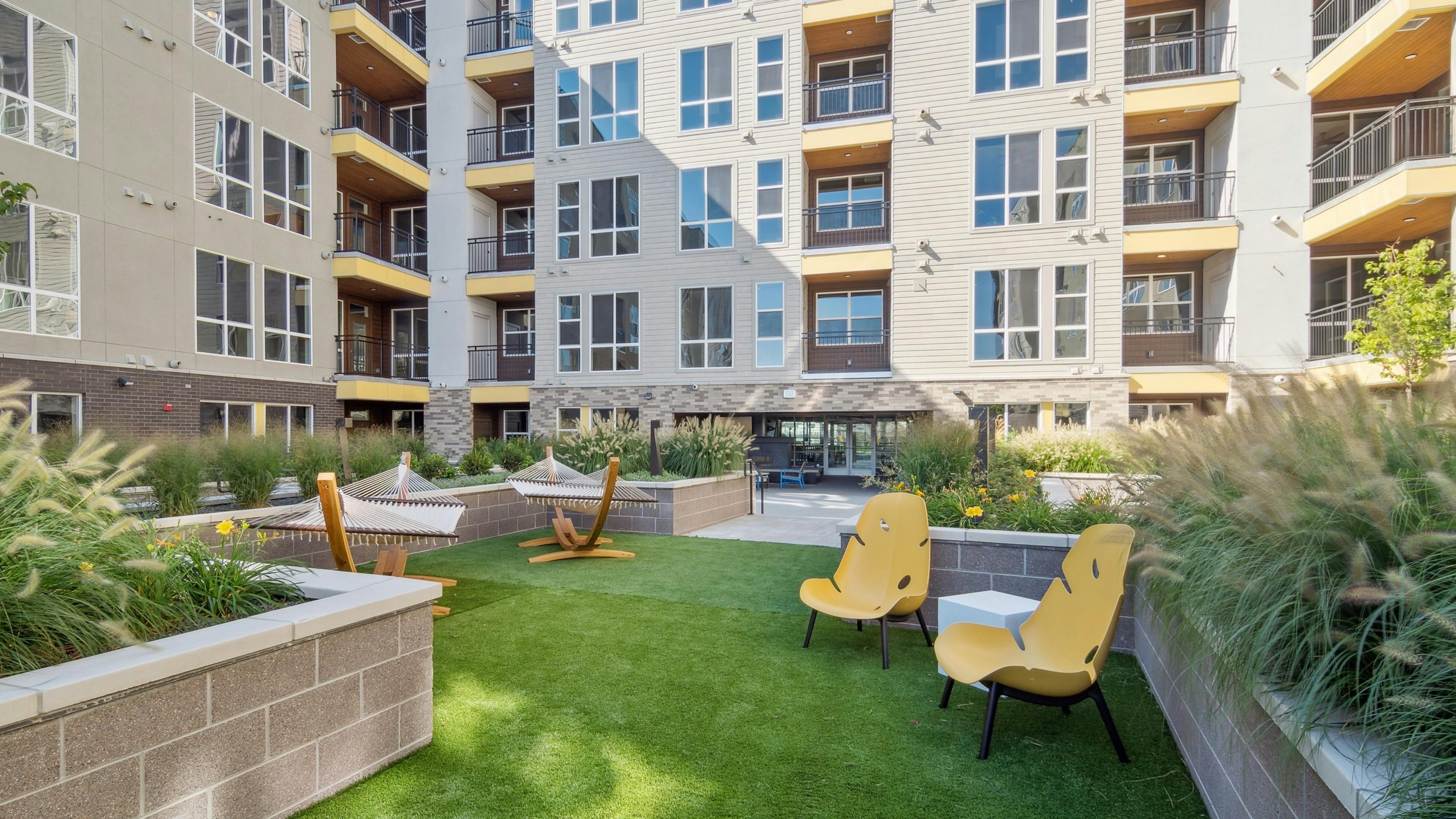 AMLI RiNo courtyard with hammocks and yellow chairs on green grass area between buildings with yellow balconies