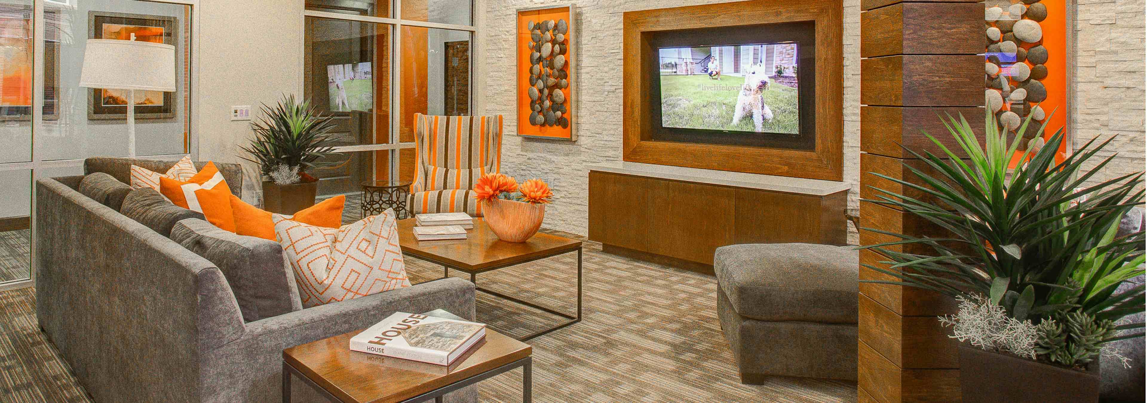 A club room at AMLI Riverfront Park apartments featuring a couch and with coffee tables and a television and green plants